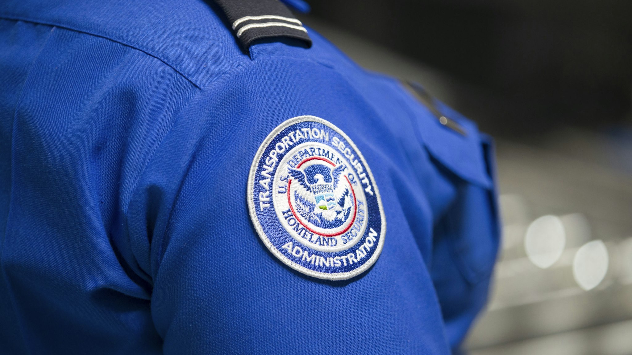 MIAMI, FLORIDA - MAY 21: A Transportation Security Administration (TSA) agent's patch is seen as she helps travelers place their bags through the 3-D scanner at the Miami International Airport on May 21, 2019 in Miami, Florida. TSA has begun using the new 3-D computed tomography (CT) scanner in a checkpoint lane to detect explosives and other prohibited items that may be inside carry-on bags. (Photo by Joe Raedle/Getty Images)