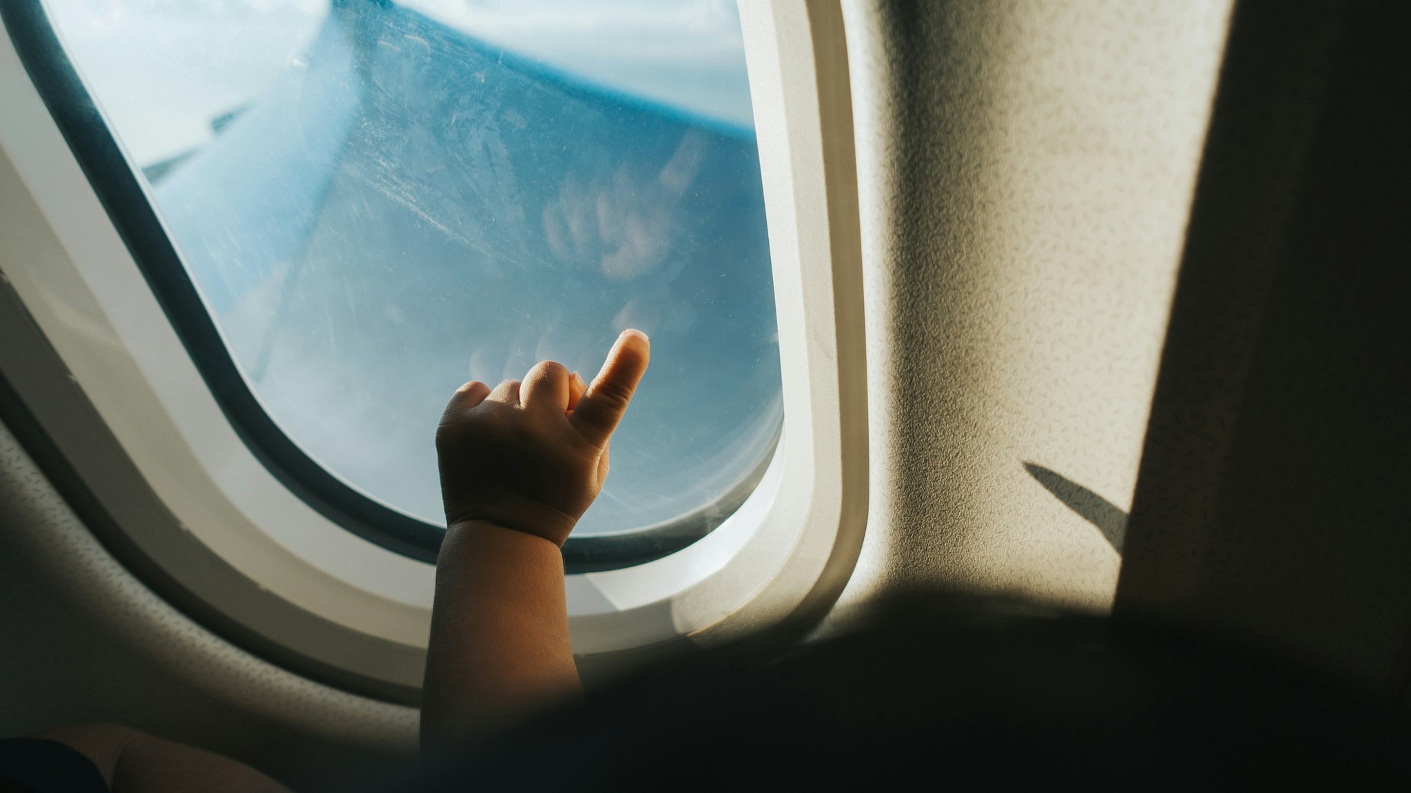 Cropped hand of a toddler pointing airplane window against blue sky while travelling - stock photo