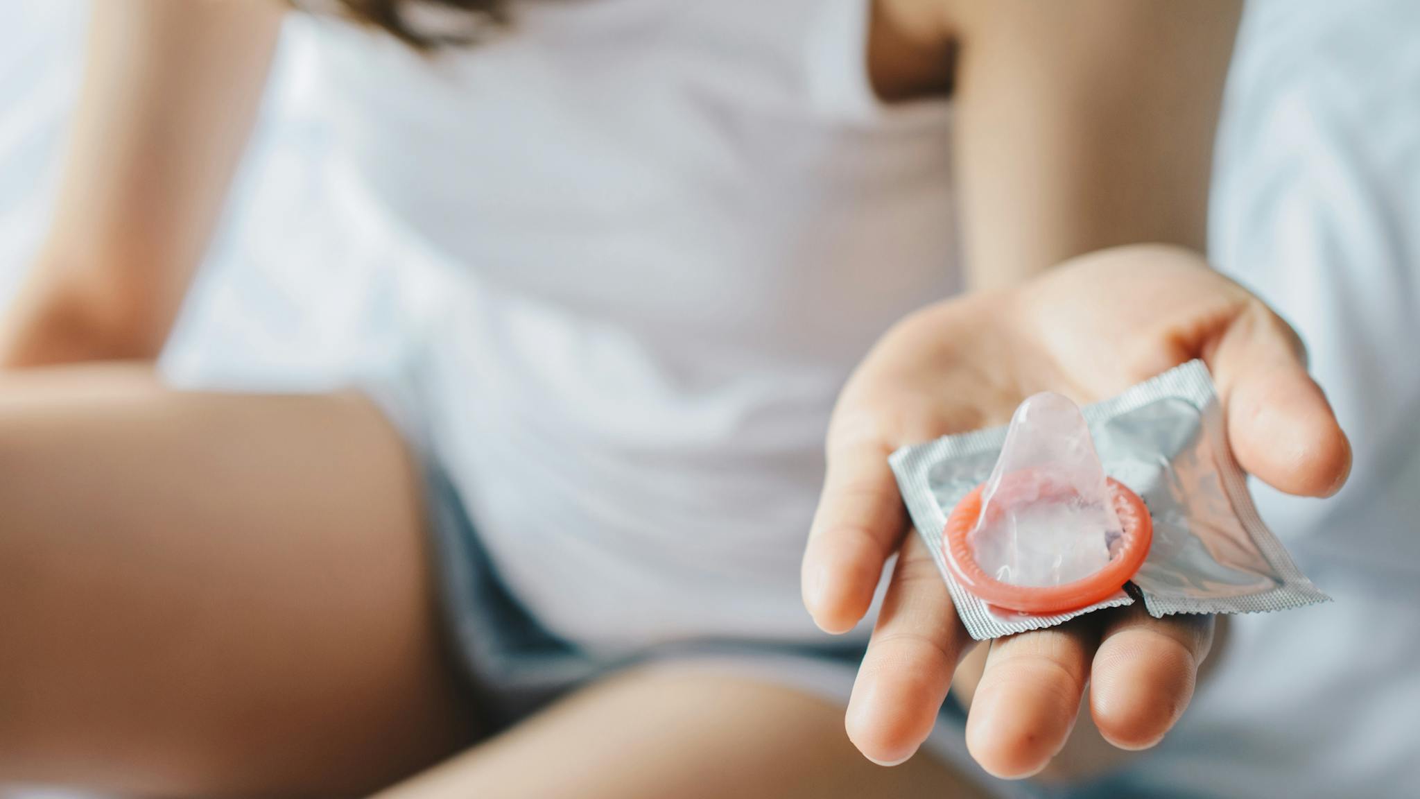 Woman Cropped shot view of woman hands holding a small condom before using it with her partner. - stock photo