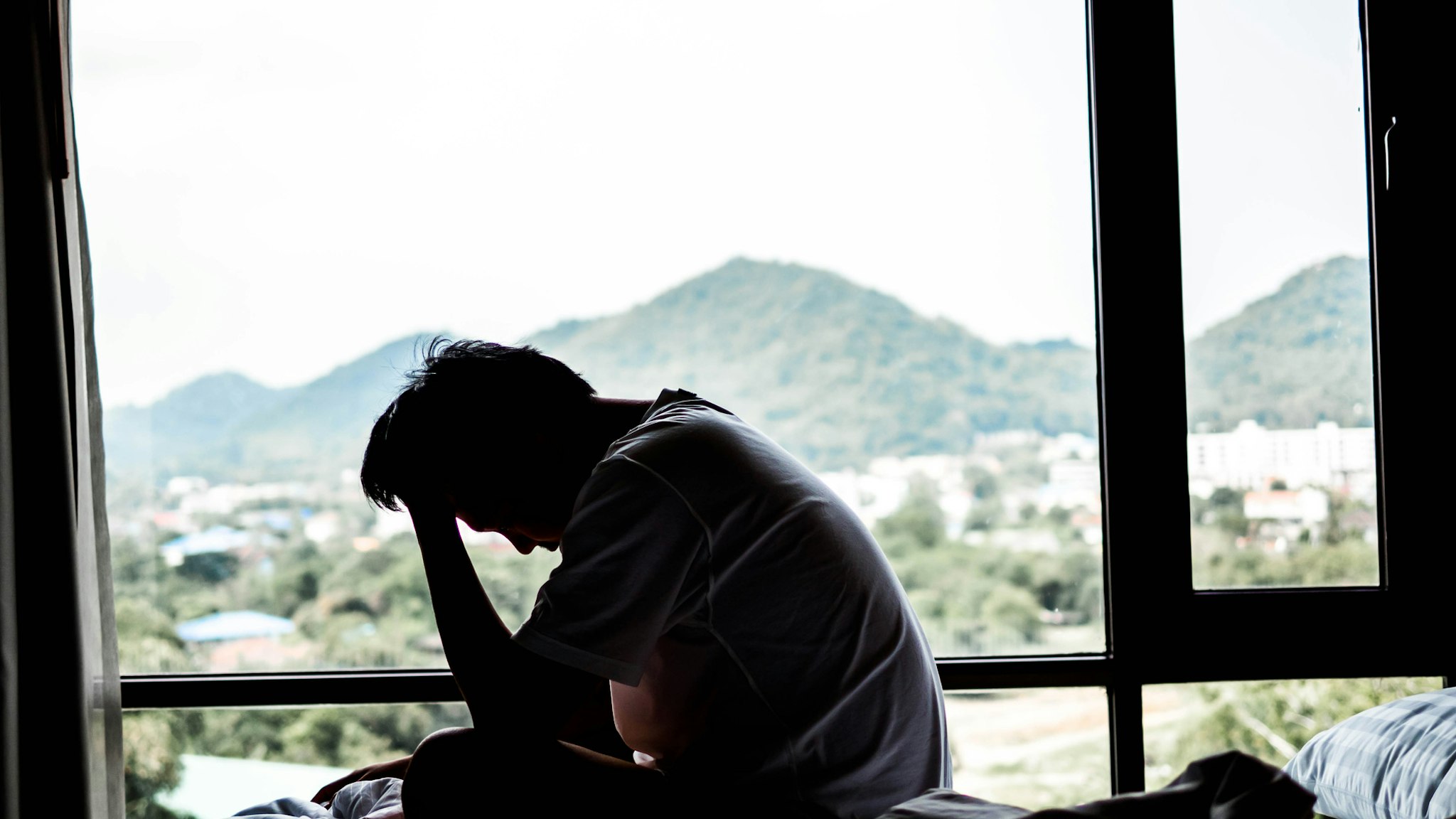 Side View Of Sad Man Sitting On Bed By Window - stock photo