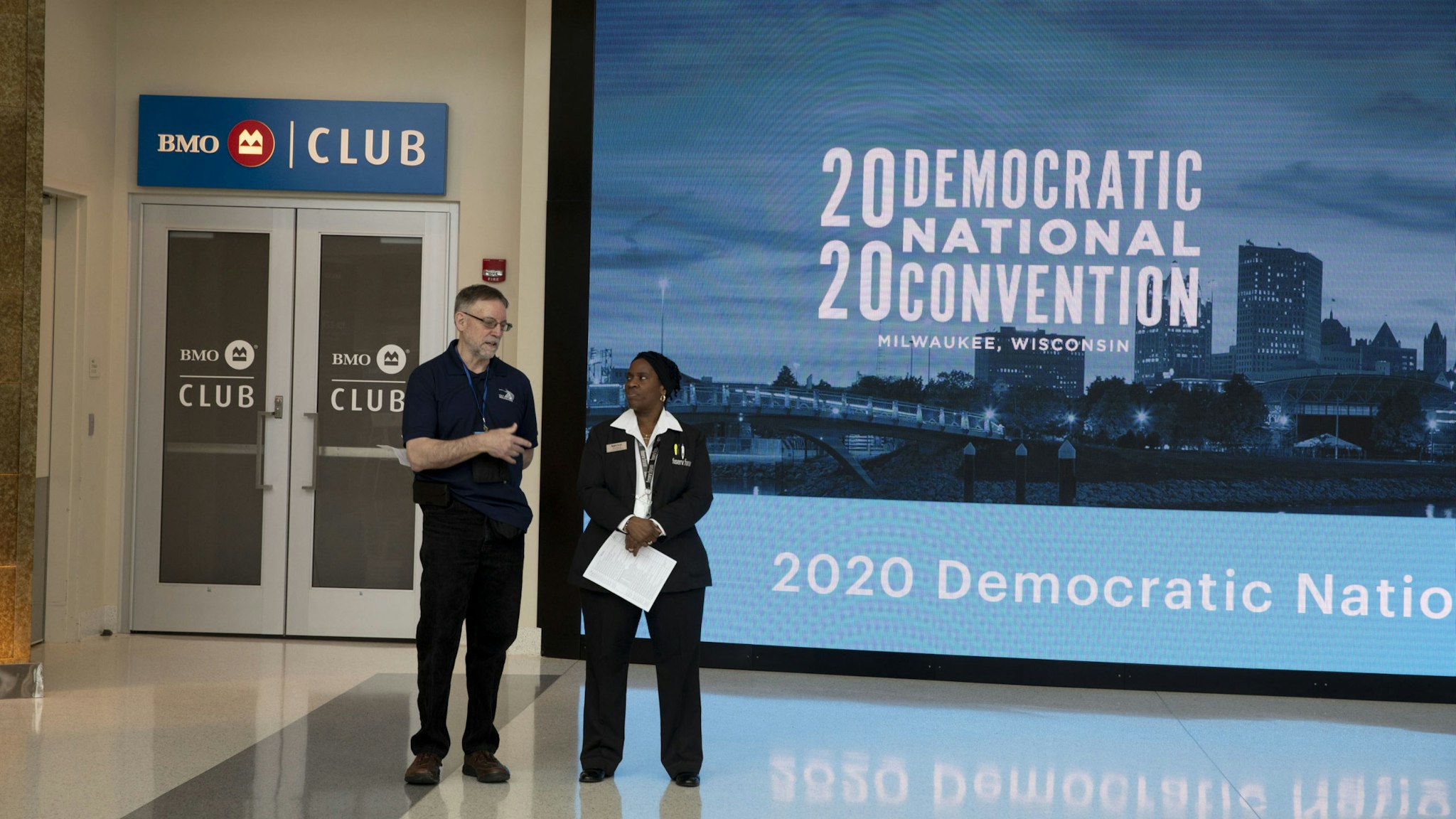 Workers stand near signage during a media walkthrough for the upcoming Democratic National Convention (DNC) at the Fiserv Forum in Milwaukee, Wisconsin, U.S., on Tuesday, Jan. 7, 2020. The 2020 DNC is scheduled to take place July 13-16. Photographer: Daniel Acker/Bloomberg via Getty Images
