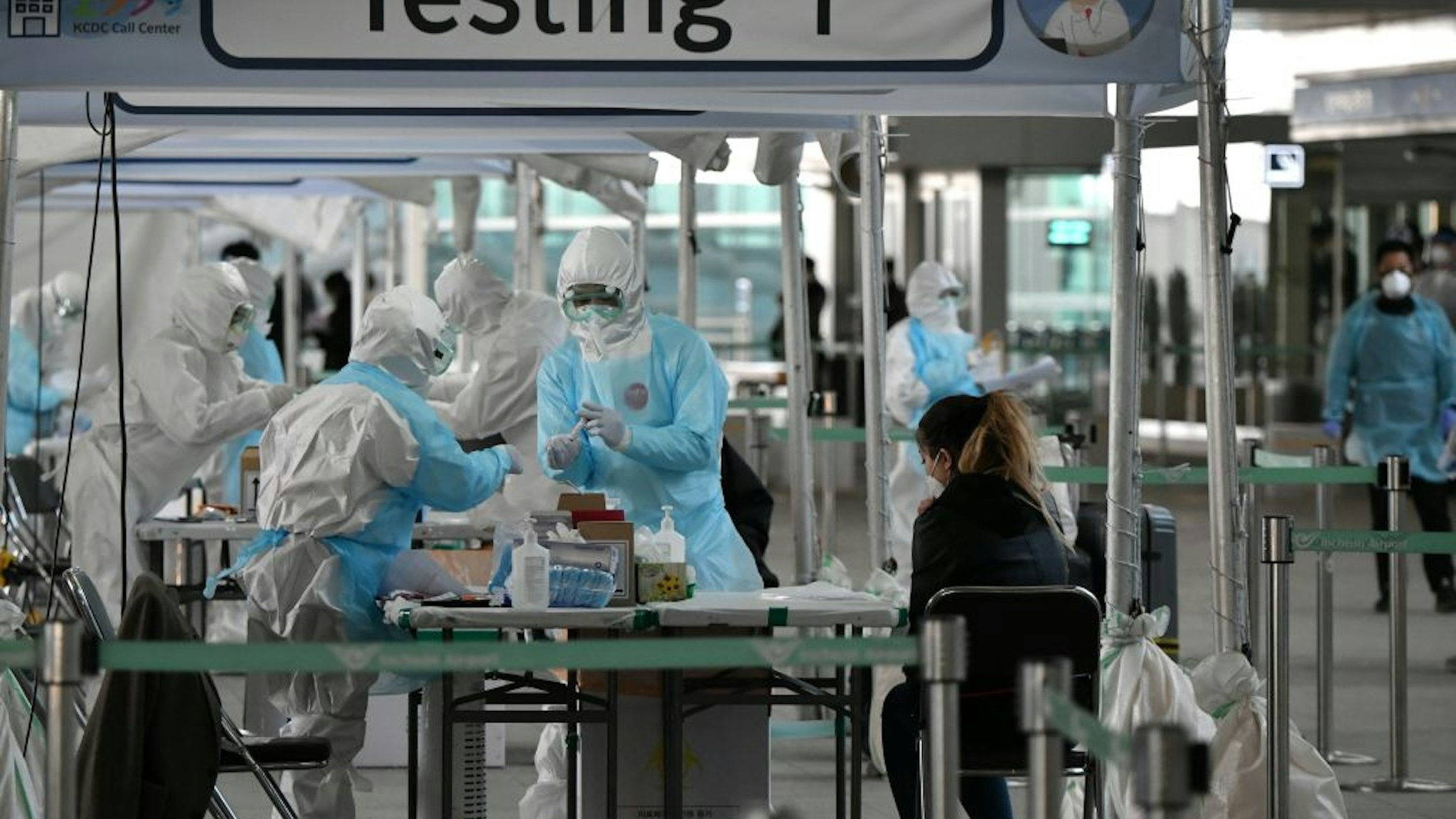 Medical staff wearing protective clothing take test samples for the COVID-19 coronavirus from a foreign passenger at a virus testing booth outside Incheon international airport, west of Seoul, on April 1, 2020.