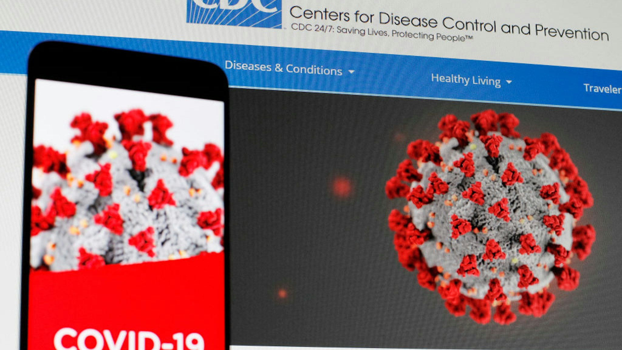 In this photo illustration the Centers of Disease Control and Prevention (CDC) web page displayed in internet on a pc screen and a coronavirus image on a mobile phone.