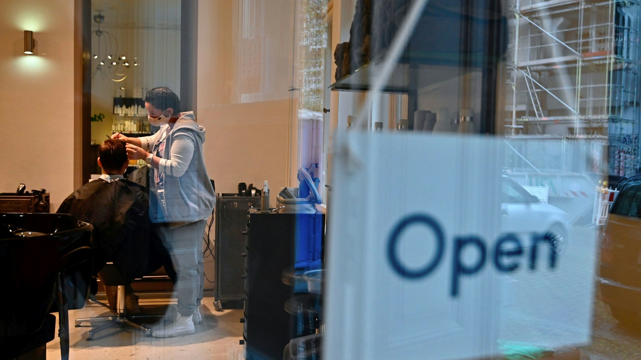 An open sign hangs in the window as a hairdresser cuts a customer's hair during the first day of reopening in Berlin on May 4, 2020 amid the novel coronavirus COVID-19 pandemic. (Photo by Tobias Schwarz / AFP) (Photo by TOBIAS SCHWARZ/AFP via Getty Images)