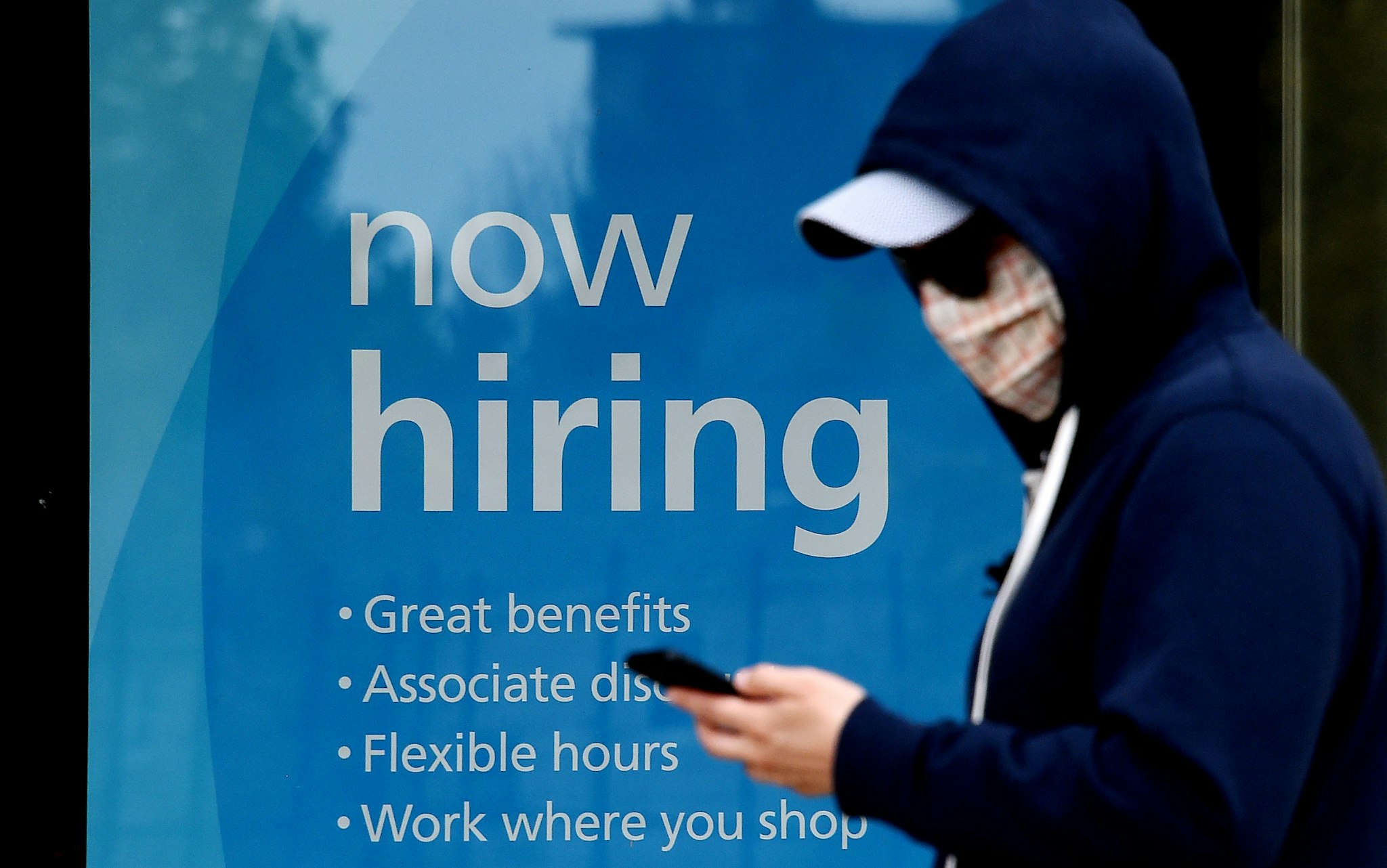 A man wearing a face mask walks past a sign "Now Hiring" in front of a store amid the coronavirus pandemic on May 14, 2020 in Arlington, Virginia. - Another 3 million people filed initial unemployment claims last week on a seasonally adjusted basis, according to the Department of Labor. (Photo by Olivier DOULIERY / AFP) (Photo by OLIVIER DOULIERY/AFP via Getty Images)