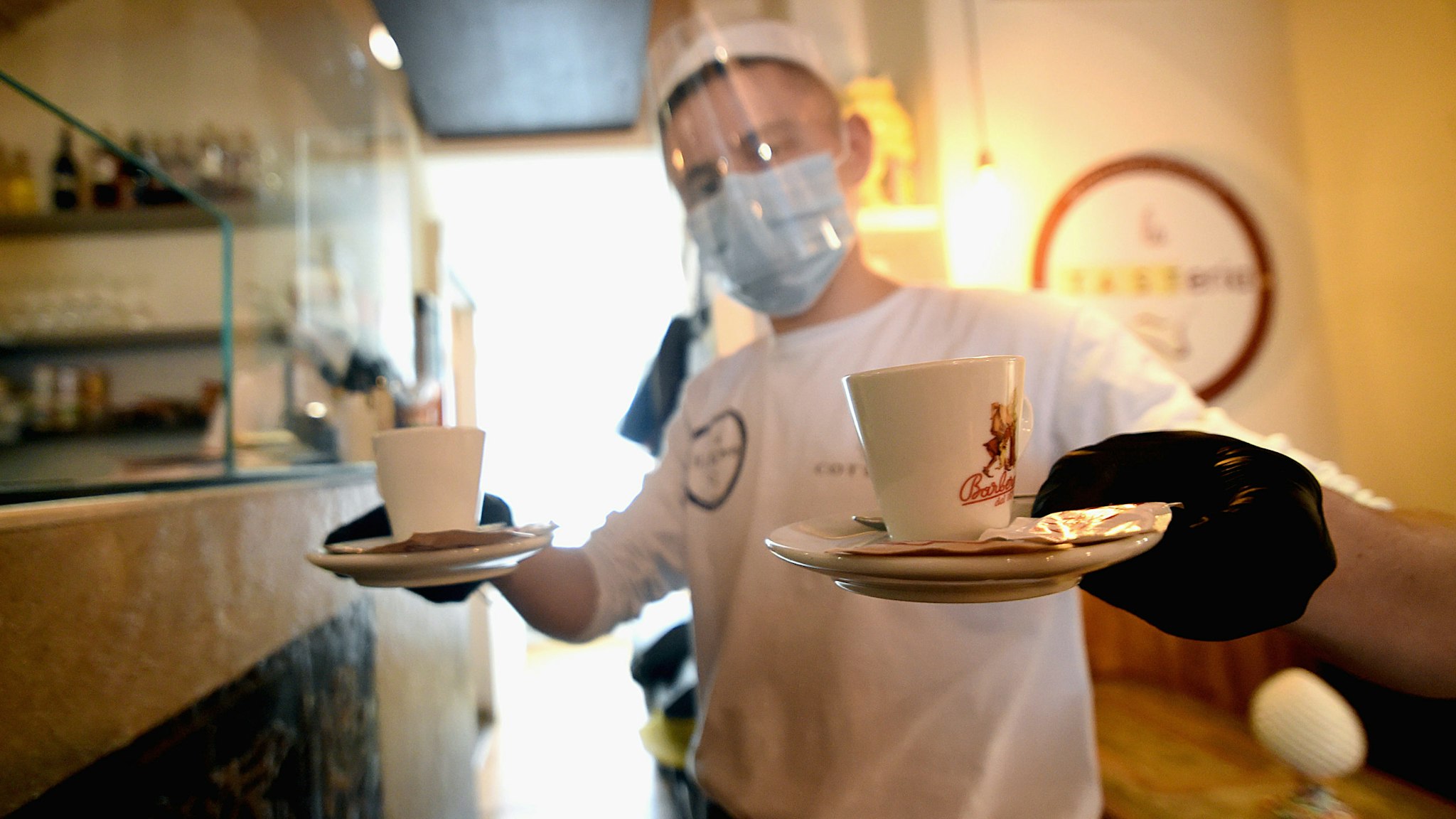 MILAN, ITALY - MAY 18: A waiter from the bistro 'La Tasteria' wearing a protective plexiglass mask brings two coffees to the table on May 18, 2020 in Milan, Italy. Restaurants, bars, cafes, hairdressers and other shops have reopened, subject to social distancing measures, after more than two months of a nationwide lockdown meant to curb the spread of Covid-19. (Photo by Pier Marco Tacca/Getty Images)