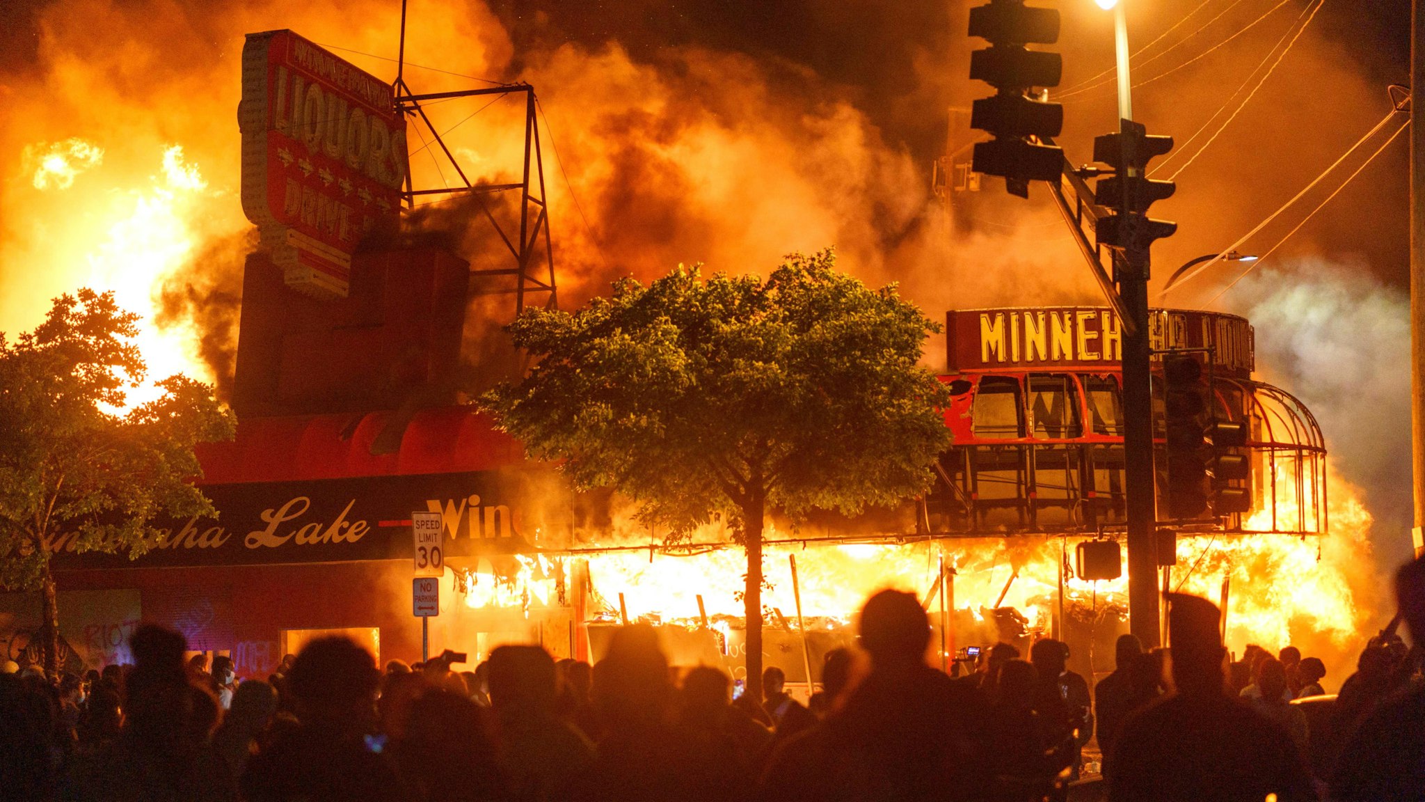 TOPSHOT - Protesters gather in front of a liquor store in flames near the Third Police Precinct on May 28, 2020 in Minneapolis, Minnesota, during a protest over the death of George Floyd, an unarmed black man, who died after a police officer kneeled on his neck for several minutes. - A police precinct in Minnesota went up in flames late on May 28 in a third day of demonstrations as the so-called Twin Cities of Minneapolis and St. Paul seethed over the shocking police killing of a handcuffed black man. The precinct, which police had abandoned, burned after a group of protesters pushed through barriers around the building, breaking windows and chanting slogans. A much larger crowd demonstrated as the building went up in flames.