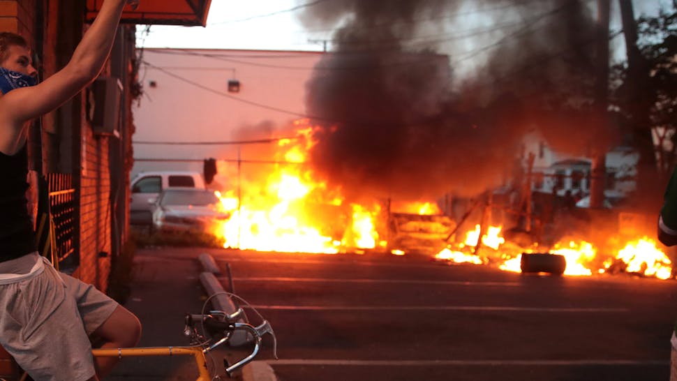MINNEAPOLIS, MINNESOTA - MAY 29: A man sits on a bicycle near burning vehicles during a protest sparked by the death of George Floyd while he was in police custody on May 29, 2020 in Minneapolis, Minnesota. Earlier today, former Minneapolis police officer Derek Chauvin was taken into custody for Floyd's death. Chauvin has been accused of kneeling on Floyd's neck as he pleaded with him about not being able to breathe. Floyd was pronounced dead a short while later. Chauvin and 3 other officers, who were involved in the arrest, were fired from the police department after a video of the arrest was circulated.