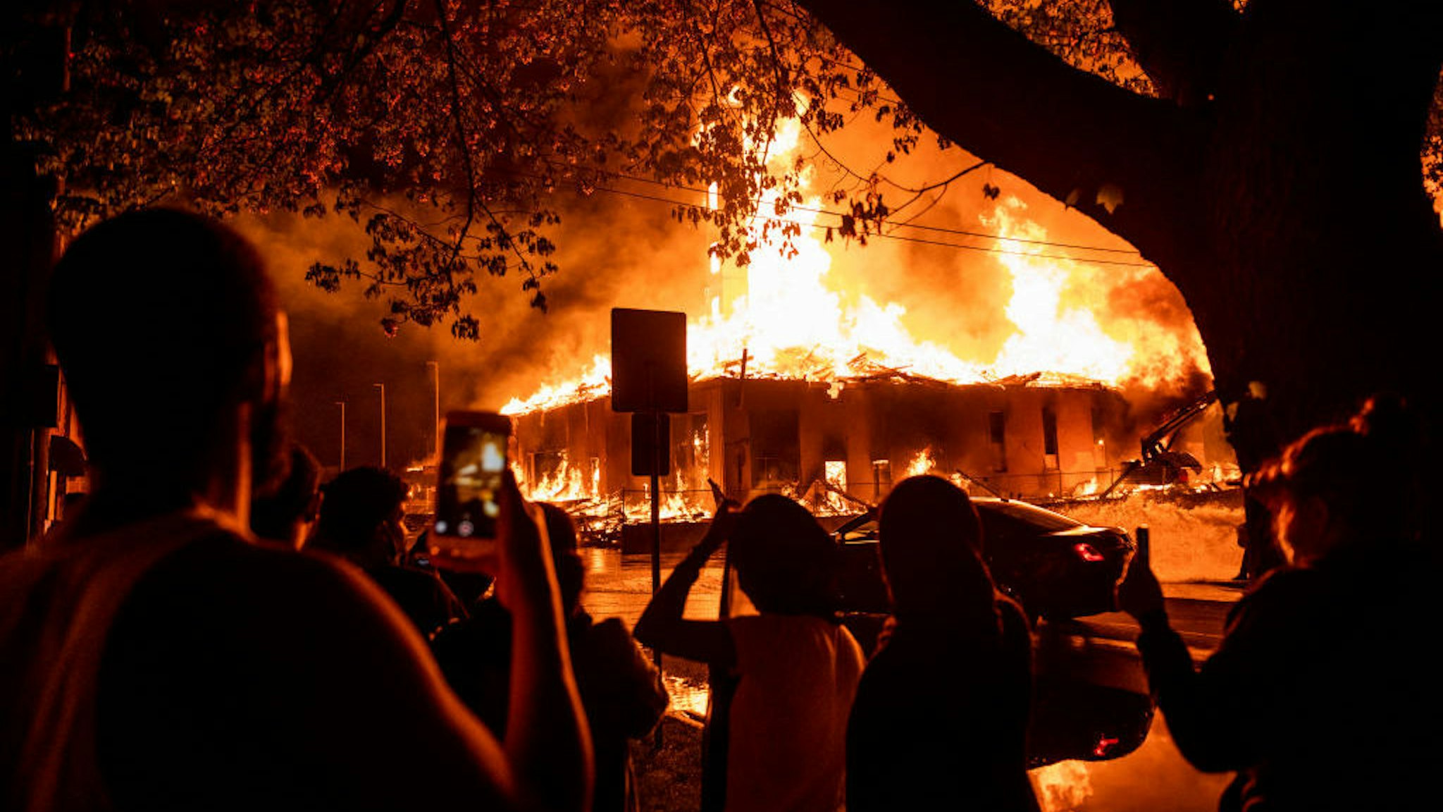 People look on as a construction site burns in a large fire near the Third Police Precinct on May 27, 2020 in Minneapolis, Minnesota. A number of businesses and homes were damaged as the area has become the site of an ongoing protest after the police killing of George Floyd. Four Minneapolis police officers have been fired after a video taken by a bystander was posted on social media showing Floyd's neck being pinned to the ground by an officer as he repeatedly said, "I can‚Äôt breathe". Floyd was later pronounced dead while in police custody after being transported to Hennepin County Medical Center. (Photo by Stephen Maturen/Getty Images)