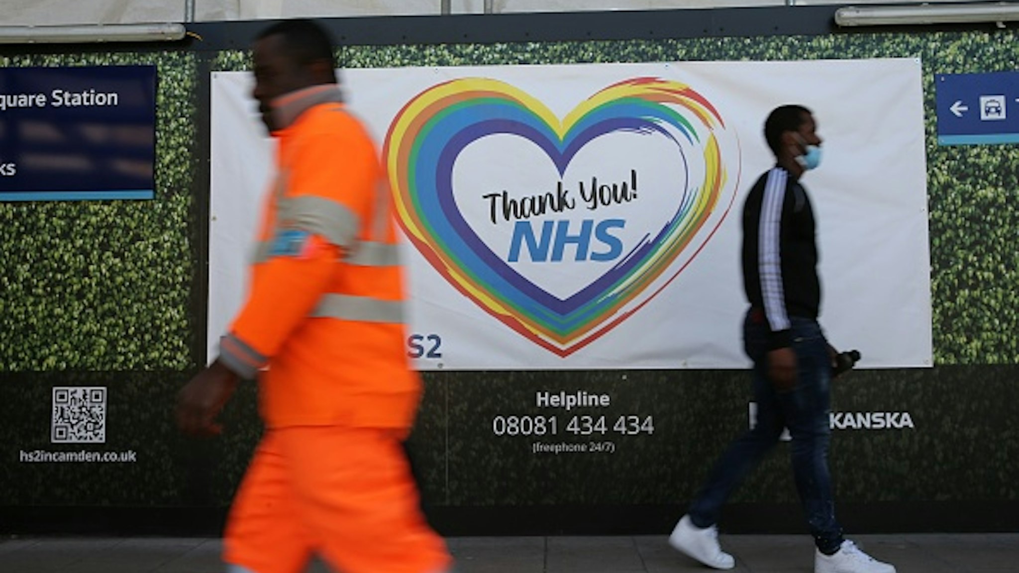 Two men walk past a sign thanking members of the NHS who continue to work during the COVID-19 outbreak at the HS2 building site near Euston in London on May 6, 2020 as life continues under a nationwide lockdown imposed to slow the spread of the novel coronavirus. - Cross-Channel train operator Eurostar on May 2 said face masks covering the mouth and nose would be compulsory on services between London, Paris and Brussels from May 4. Britain's death toll from the coronavirus has topped 32,000, according to an updated official count released May 5, pushing the country past Italy to become the second-most impacted after the United States.