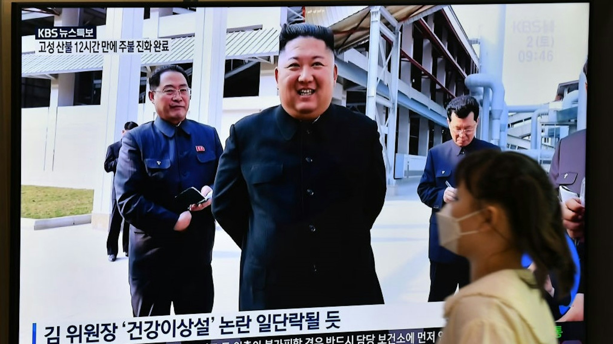 TOPSHOT - A woman walks past a television news screen showing a picture of North Korean leader Kim Jong Un attending a ceremony to mark the completion of Sunchon phosphatic fertiliser factory, at a railway station in Seoul on May 2, 2020. - North Korea's Kim Jong Un has made his first public appearance in nearly three weeks, state media reported on May 2, following intense speculation that the leader of the nuclear-armed nation was seriously ill or possibly dead. (Photo by Jung Yeon-je / AFP) (Photo by