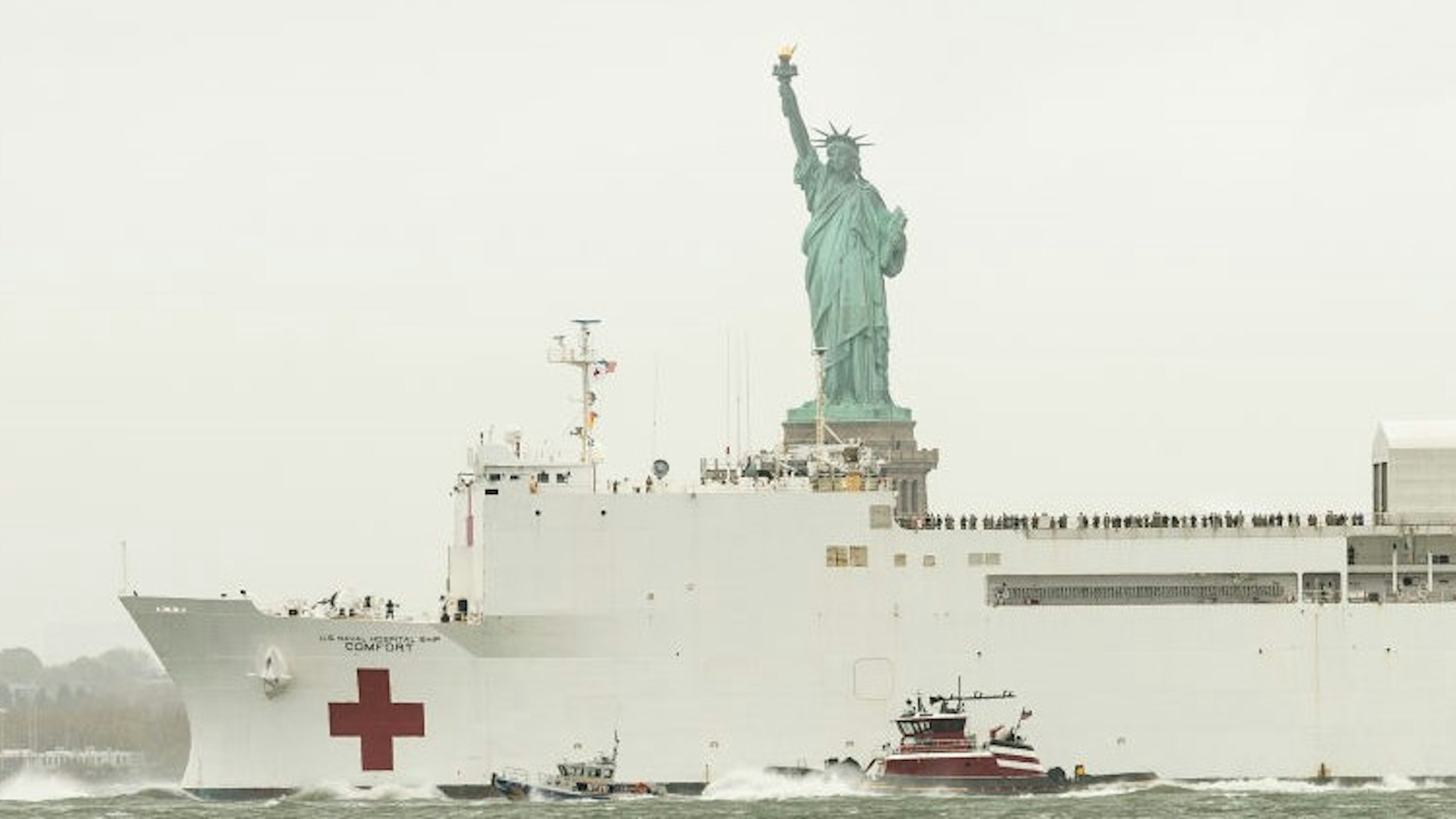 NEW YORK, UNITED STATES - 2020/04/30: On a gloomy rainy day USNS Comfort hospital ship leaves New York City in front of Statue of Liberty after treating some patients during COVID-19 pandemic. (Photo by