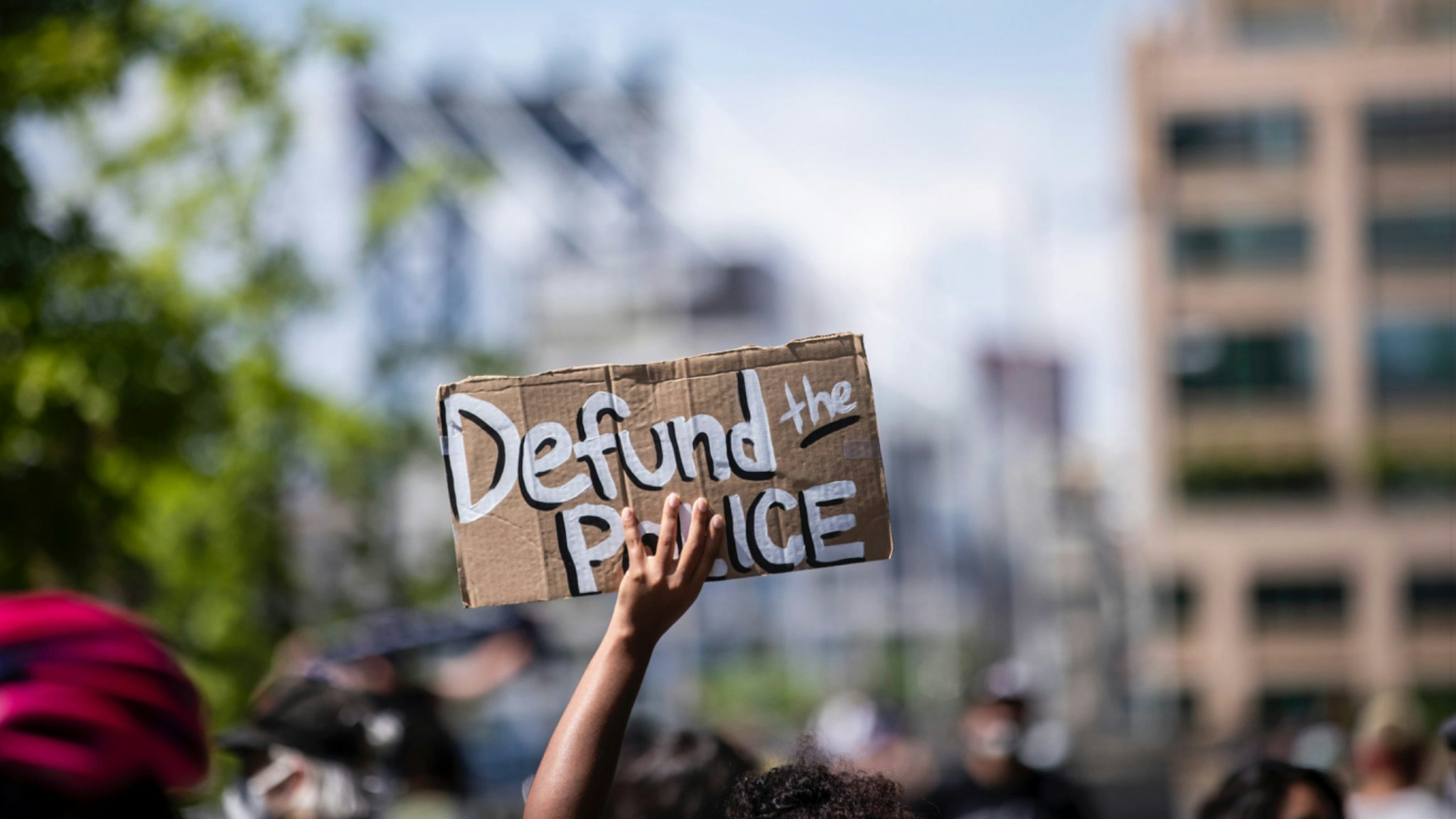 MANHATTAN, NY - JUNE 19: A protester holds up a homemade sign that says, "Defund the Police" with the Manhattan Bridge behind them as they perform a peaceful protest walk across the Brooklyn Bridge.