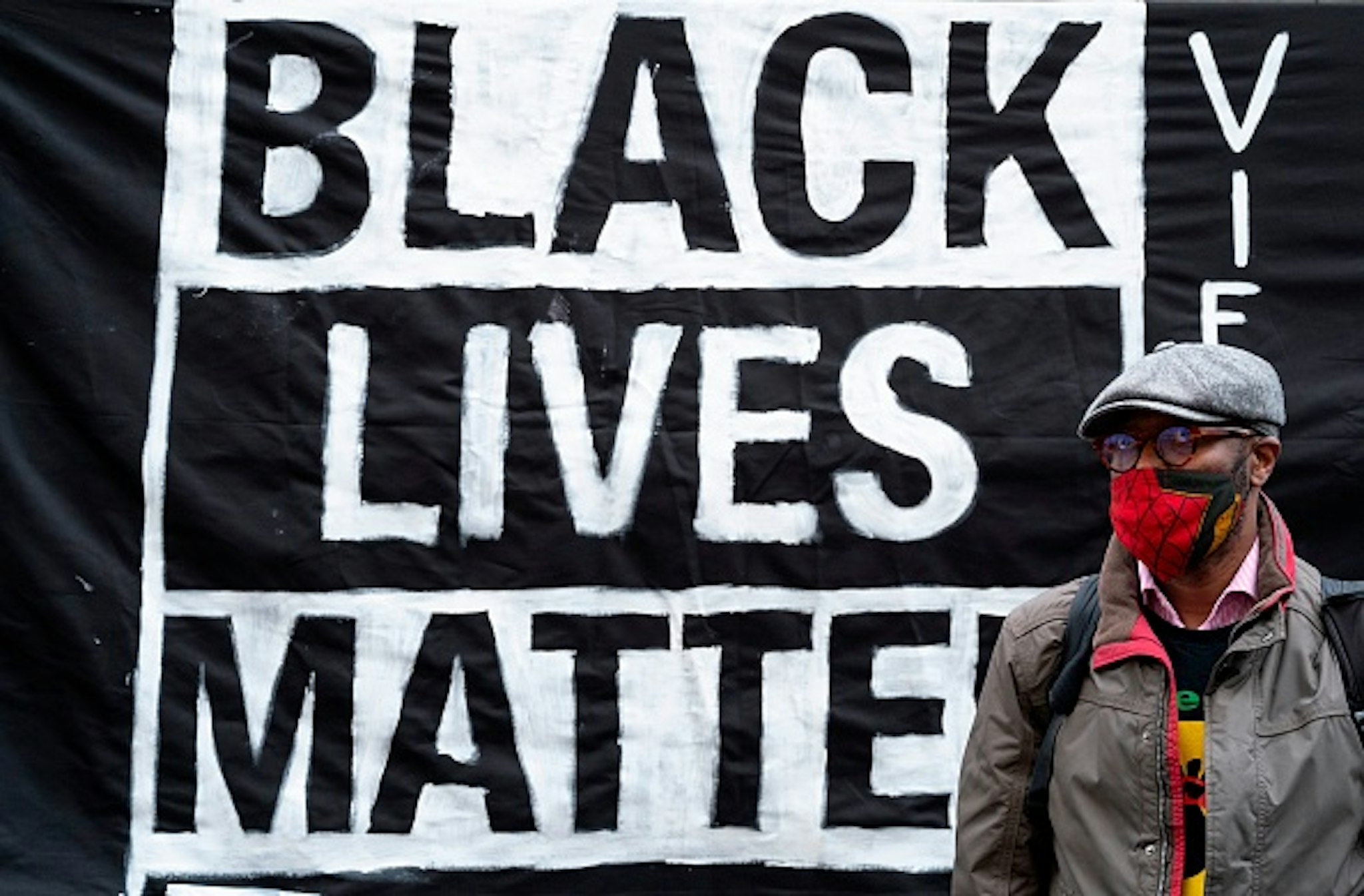 A protestor stands in front of a banner during a demonstration on June 5, 2020 outside the US embassy in Vienna, Austria, to show solidarity with the Black Lives Matter movement in the wake of the killing of George Floyd, an unarmed black man who died after a police officer knelt on his neck in Minneapolis. - Hundreds of mourners joined an emotional memorial service in Minneapolis for George Floyd, the black man killed by police last week.The police killing of George Floyd led to diverse protests calling for an end to violence towards African Americans, whom studies have found face an elevated risk of dying at the hands of law enforcement
