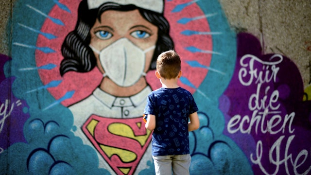 TOPSHOT - A boy stands in front of a graffiti painted by artist Kai 'Uzey' Wohlgemuth featuring a nurse as Superwoman on a wall in Hamm, western Germany, on April 8, 2020 refering to the spread of the novel coronavirus COVID-19.