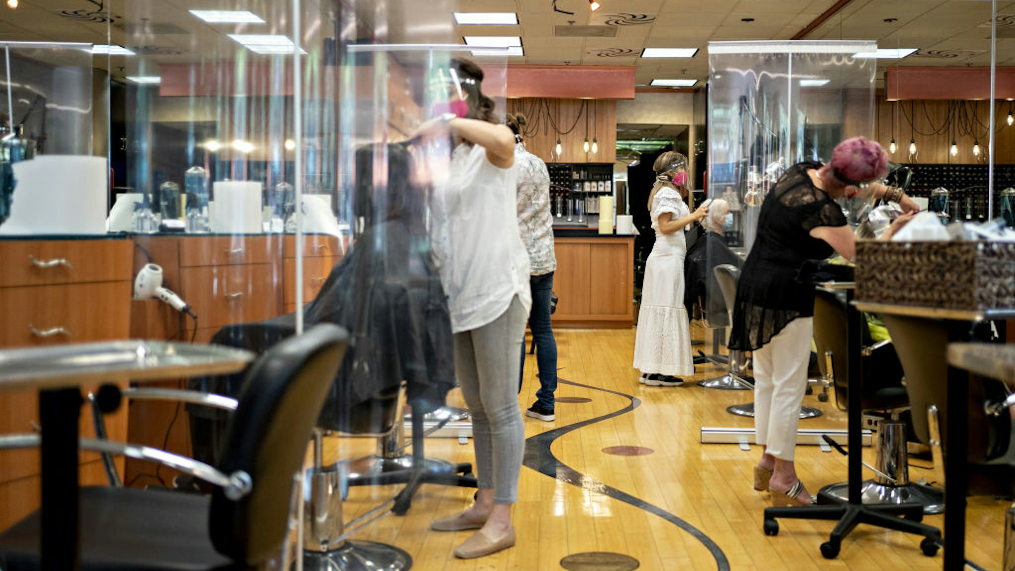 Stylists work behind plastic dividers at a hair salon in Arlington, Virginia, U.S., on Friday, May 29, 2020.