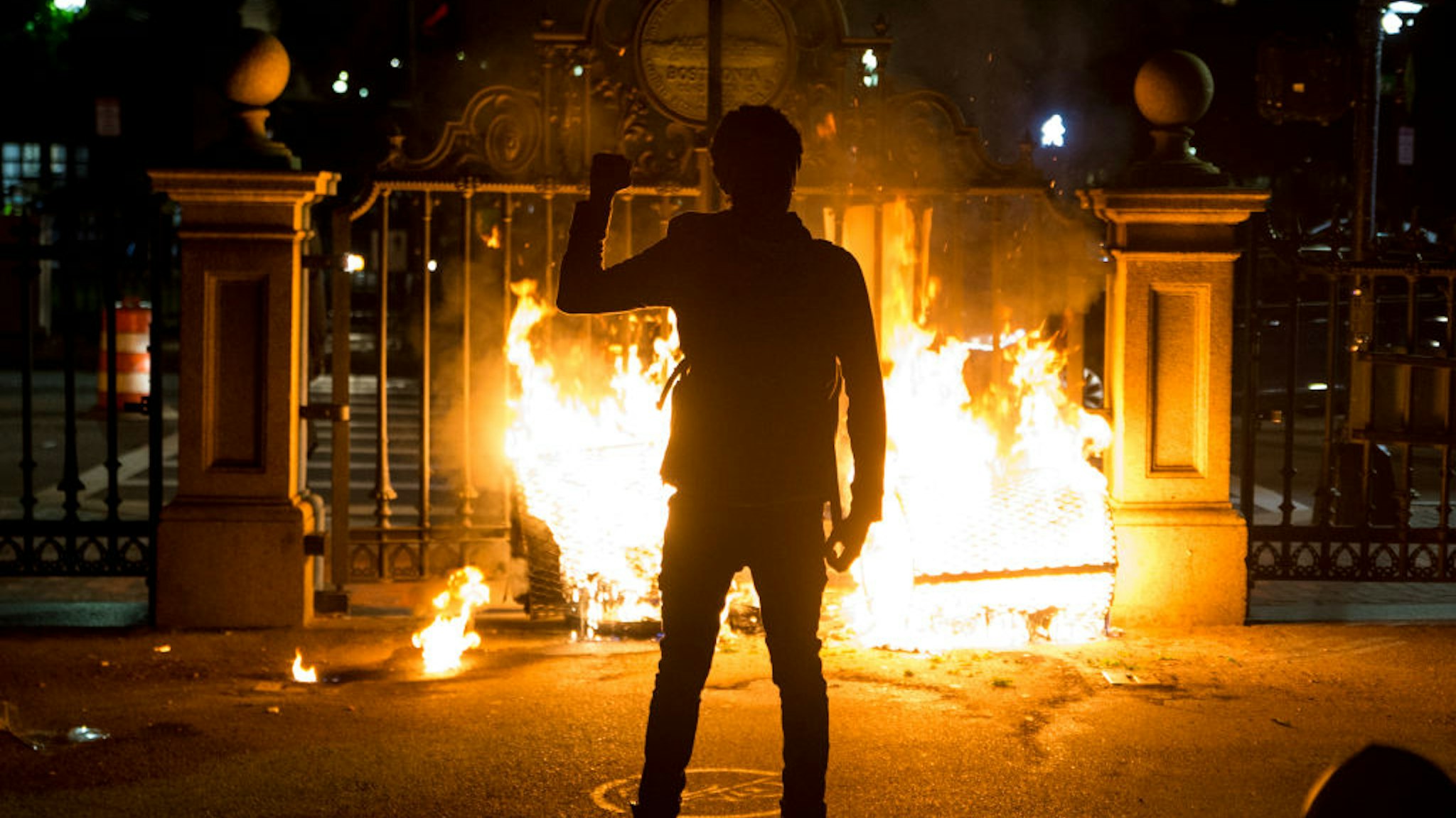 A protester holds up a fist in front of the burning gate of the Boston Public Garden as protestors try to barricade the police out as they get pushed through the Boston Commons on May 31, 2020.