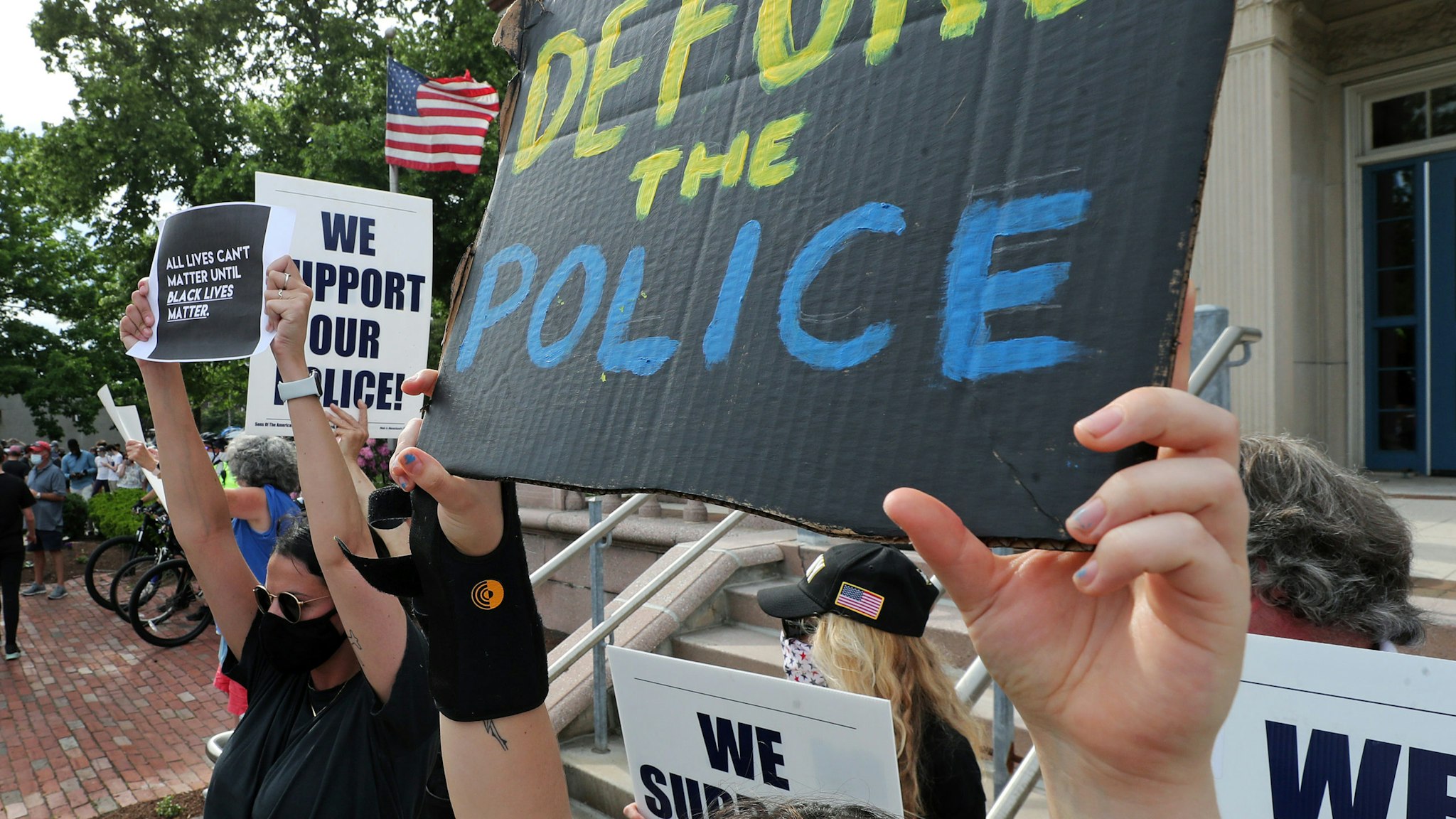 BOSTON, MA - JUNE 4: A person holding a sign reading "defund the police" stands next to a counter protester holding a "we support our police sign" in front of the Newton Police Headquarters in Newton, MA on June 4, 2020. Protesters gather and march calling for justice for George Floyd and other Black Americans killed by police officers on the day of Floyd's funeral. (Photo by Jim Davis/The Boston Globe via Getty Images)