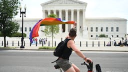Supreme Court A man waves a rainbow flag as he rides by the US Supreme Court that released a decision that says federal law protects LGBTQ workers from discrimination on June 15, 2020 in Washington,DC. - The US top court has ruled it illegal to fire workers based on sexual orientation. (Photo by JIM WATSON / AFP) (Photo by JIM WATSON/AFP via Getty Images)