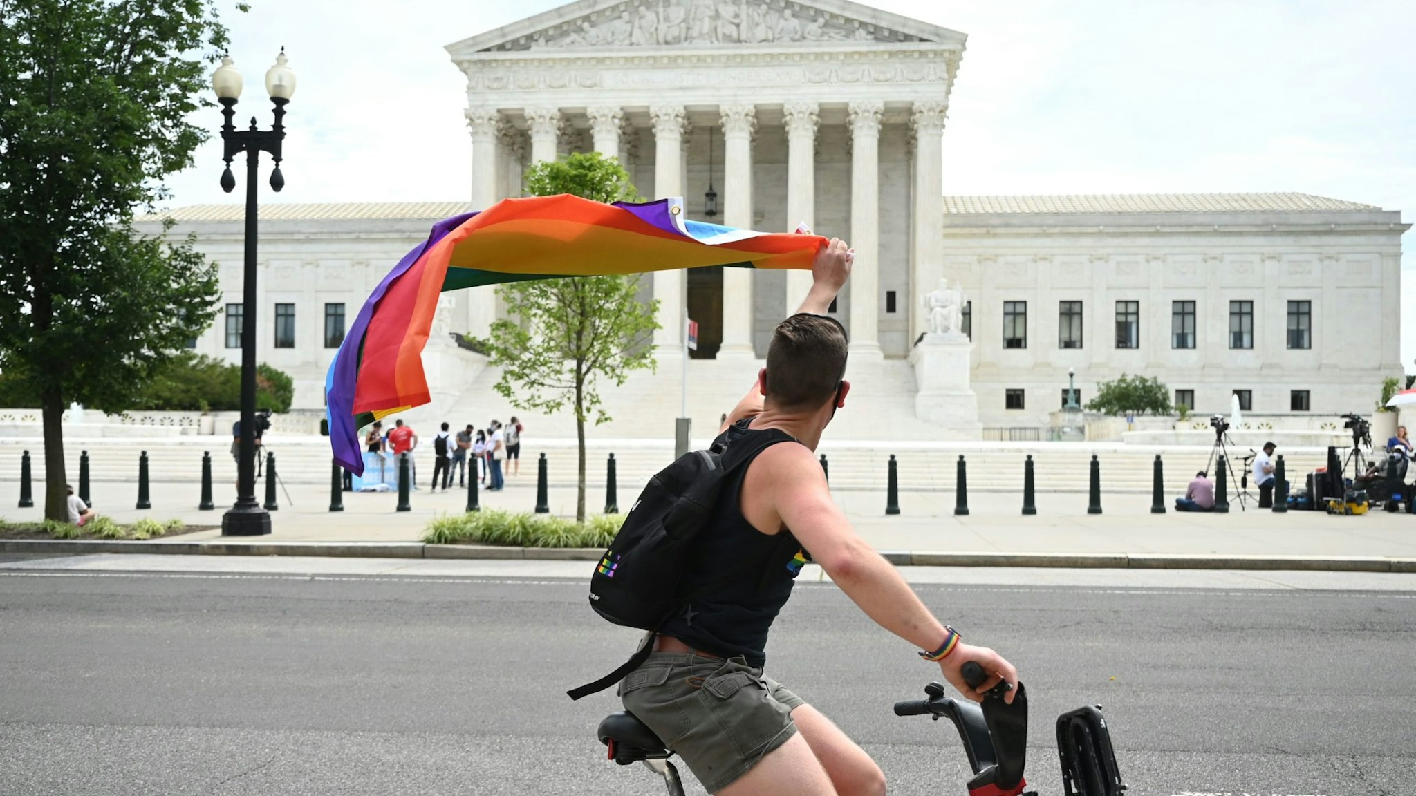 A man waves a rainbow flag as he rides by the US Supreme Court that released a decision that says federal law protects LGBTQ workers from discrimination on June 15, 2020 in Washington,DC. - The US top court has ruled it illegal to fire workers based on sexual orientation. (Photo by JIM WATSON / AFP) (Photo by JIM WATSON/AFP via Getty Images)