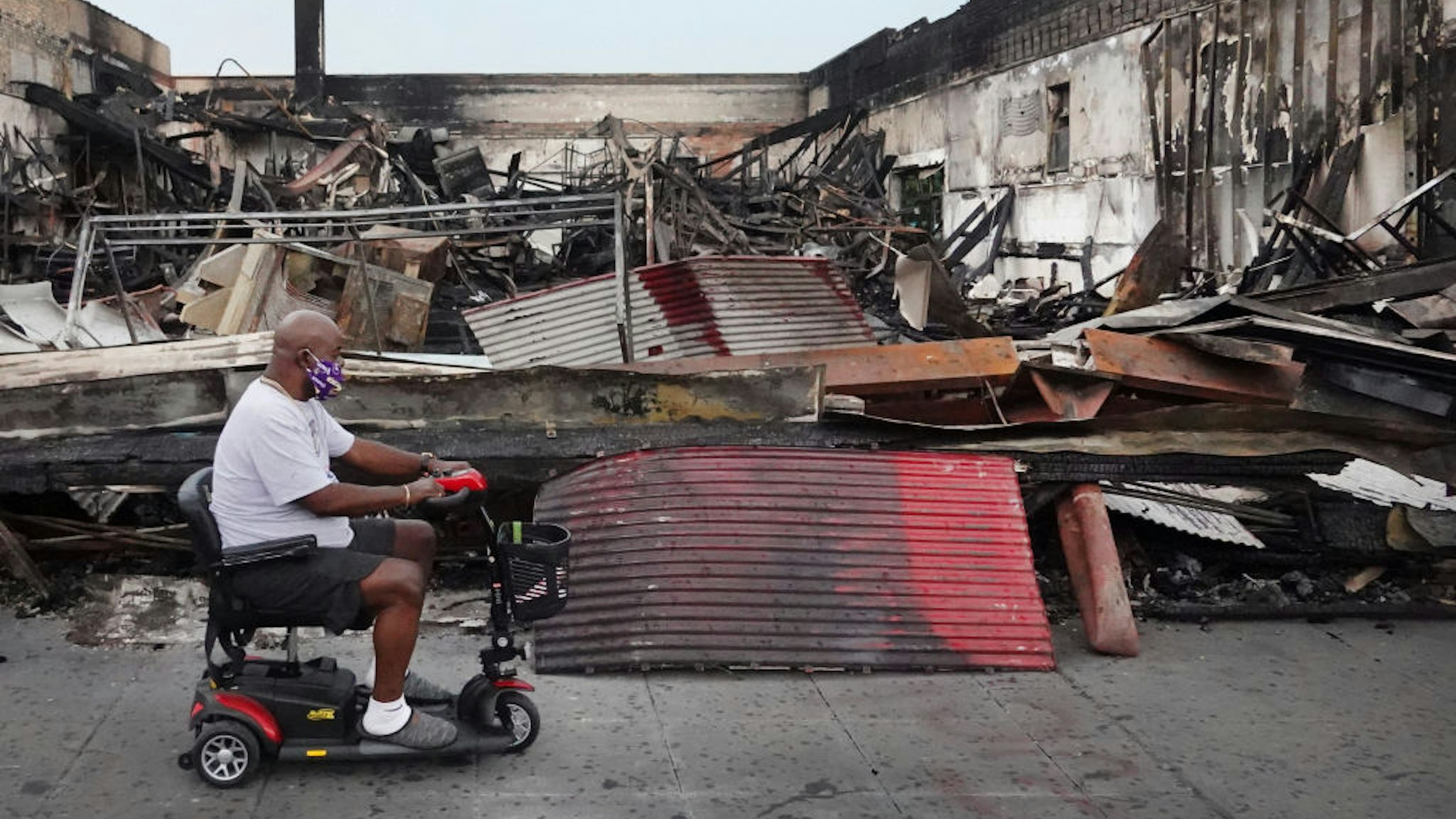 A man rides a scooter past the charred wreckage of a building after being burned to the ground during last week's rioting sparked by the death of George Floyd on June 2, 2020 in Minneapolis, Minnesota.