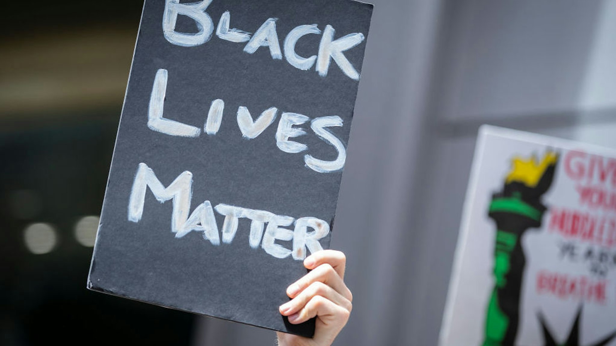 A Caucasian protester holds a handmade sign that reads, "Black Lives Matter" in a similar way to another sign with the Statue Of Liberty in Times Square.