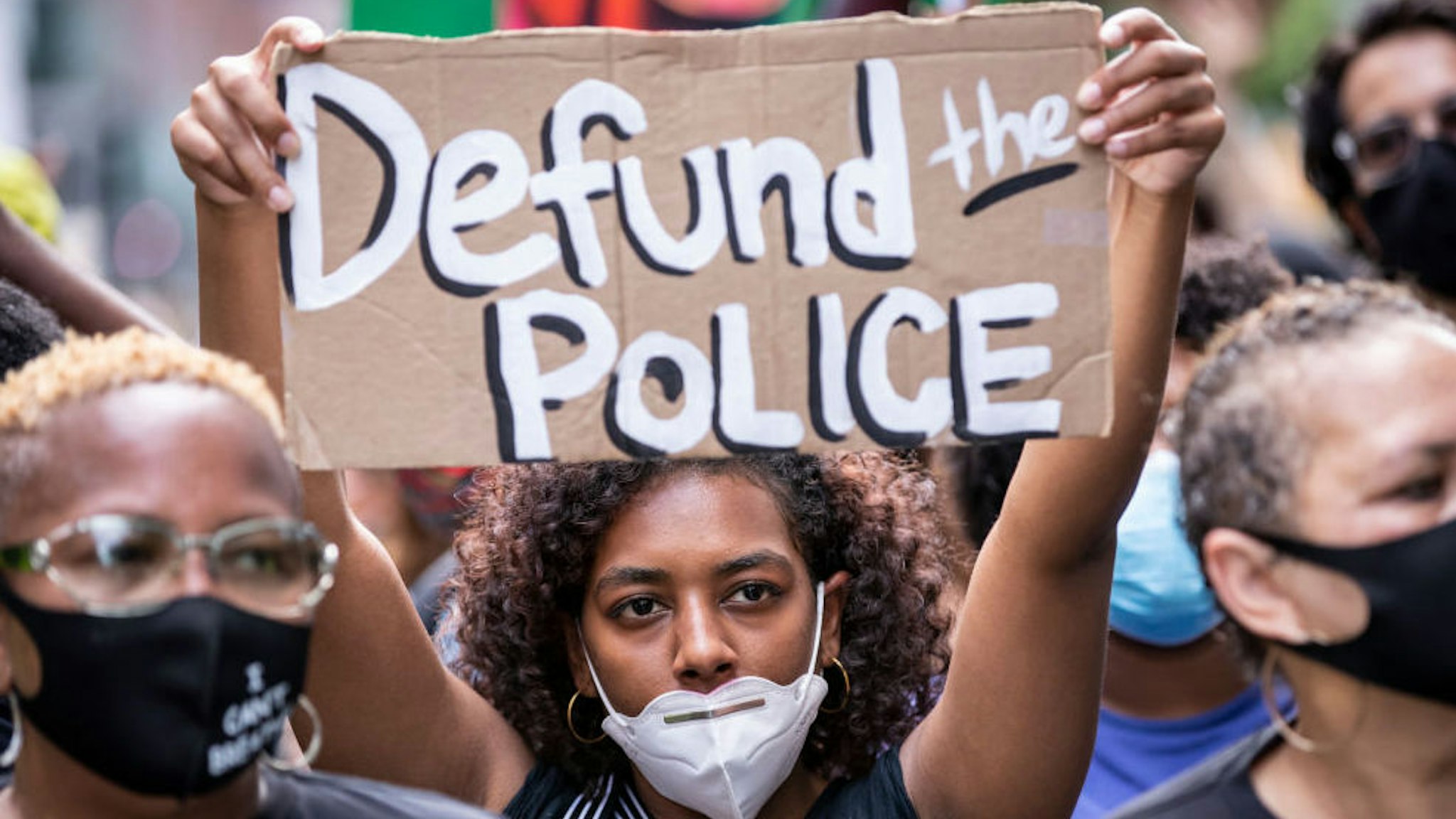 An African American protester wears a mask and holds a homemade sign that says, "Defund the Police" as they perform a peaceful protest walk across the Brooklyn Bridge.