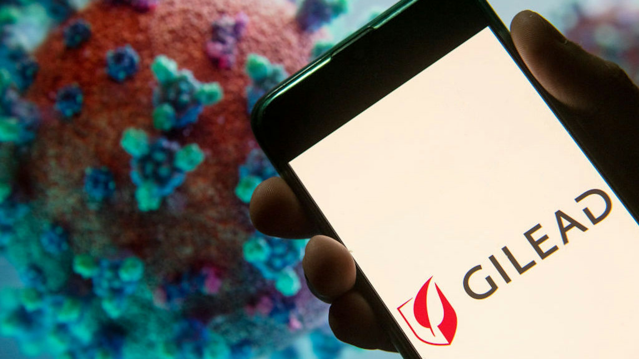 In this photo illustration the American biotechnology company Gilead Sciences logo seen displayed on a smartphone with a computer model of the COVID-19 coronavirus on the background. (Photo by Budrul Chukrut/SOPA Images/LightRocket via Getty Images)