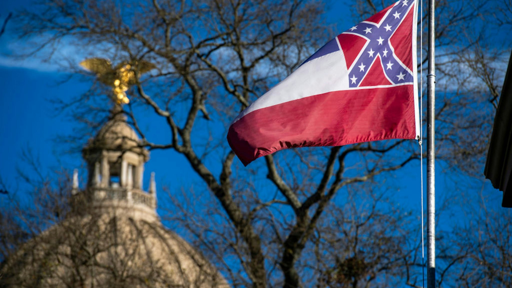 Jackson, MS - JANUARY 10: The Mississippi State Capitol dome is visible in the distance as the flag of the state of Mississippi flies nearby in Jackson, MS on January 10, 2019.
