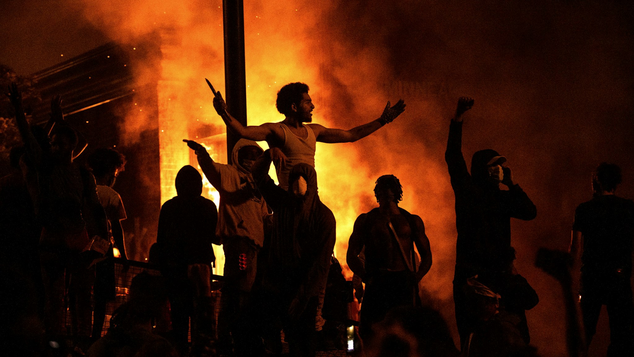 MINNEAPOLIS, MN - MAY 28: Protesters cheer as the Third Police Precinct burns behind them on May 28, 2020 in Minneapolis, Minnesota. As unrest continues after the death of George Floyd police abandoned the precinct building, allowing protesters to set fire to it.