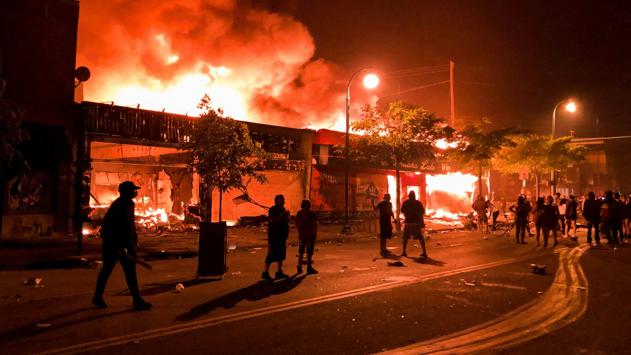 TOPSHOT - Flames rise from a liquor store and shops near the Third Police Precinct on May 28, 2020 in Minneapolis, Minnesota, during a protest over the death of George Floyd, an unarmed black man, who died after a police officer kneeled on his neck for several minutes. - A police precinct in Minnesota went up in flames late on May 28 in a third day of demonstrations as the so-called Twin Cities of Minneapolis and St. Paul seethed over the shocking police killing of a handcuffed black man. The precinct, which police had abandoned, burned after a group of protesters pushed through barriers around the building, breaking windows and chanting slogans. A much larger crowd demonstrated as the building went up in flames.