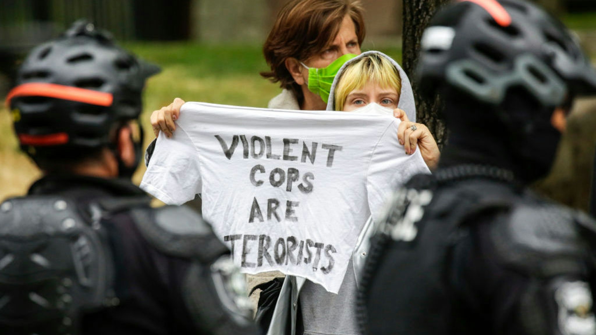 A woman holds a shirt that says "violent cops are terrorists" as Seattle Police arrested several people after demonstrators blocked an intersection outside the recently-cleared Capitol Hill Occupied Protest (CHOP) in Seattle, Washington on July 1, 2020. (Photo by Jason Redmond / AFP) (Photo by JASON REDMOND/AFP via Getty Images)