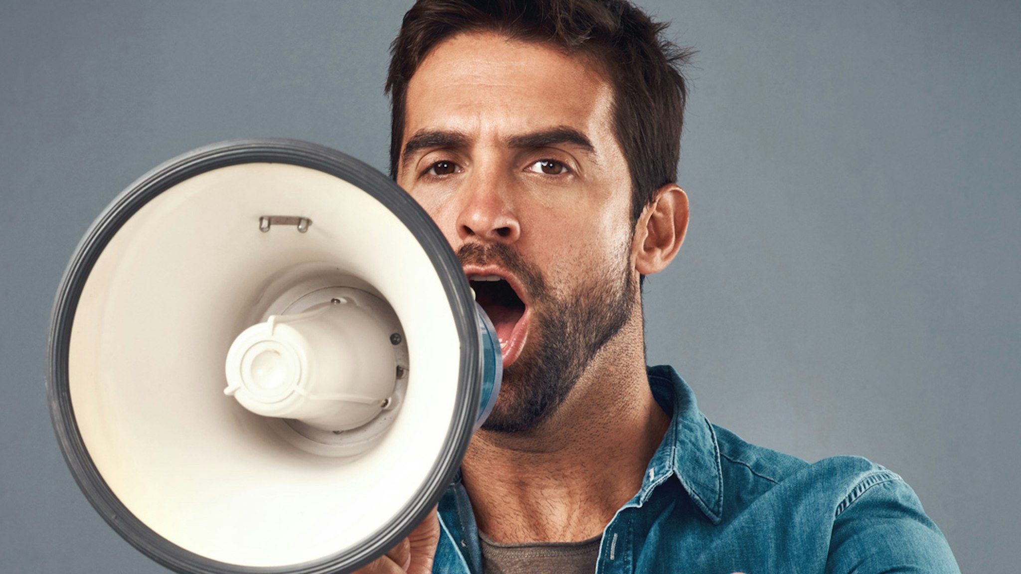 Studio shot of a handsome young man using a megaphone against a grey background