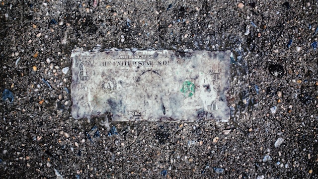 Still life of deteriorating one dollar bill on wet pavement.