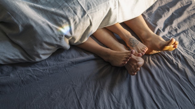 Couple's feet sticking out from under duvet in bed - stock photo