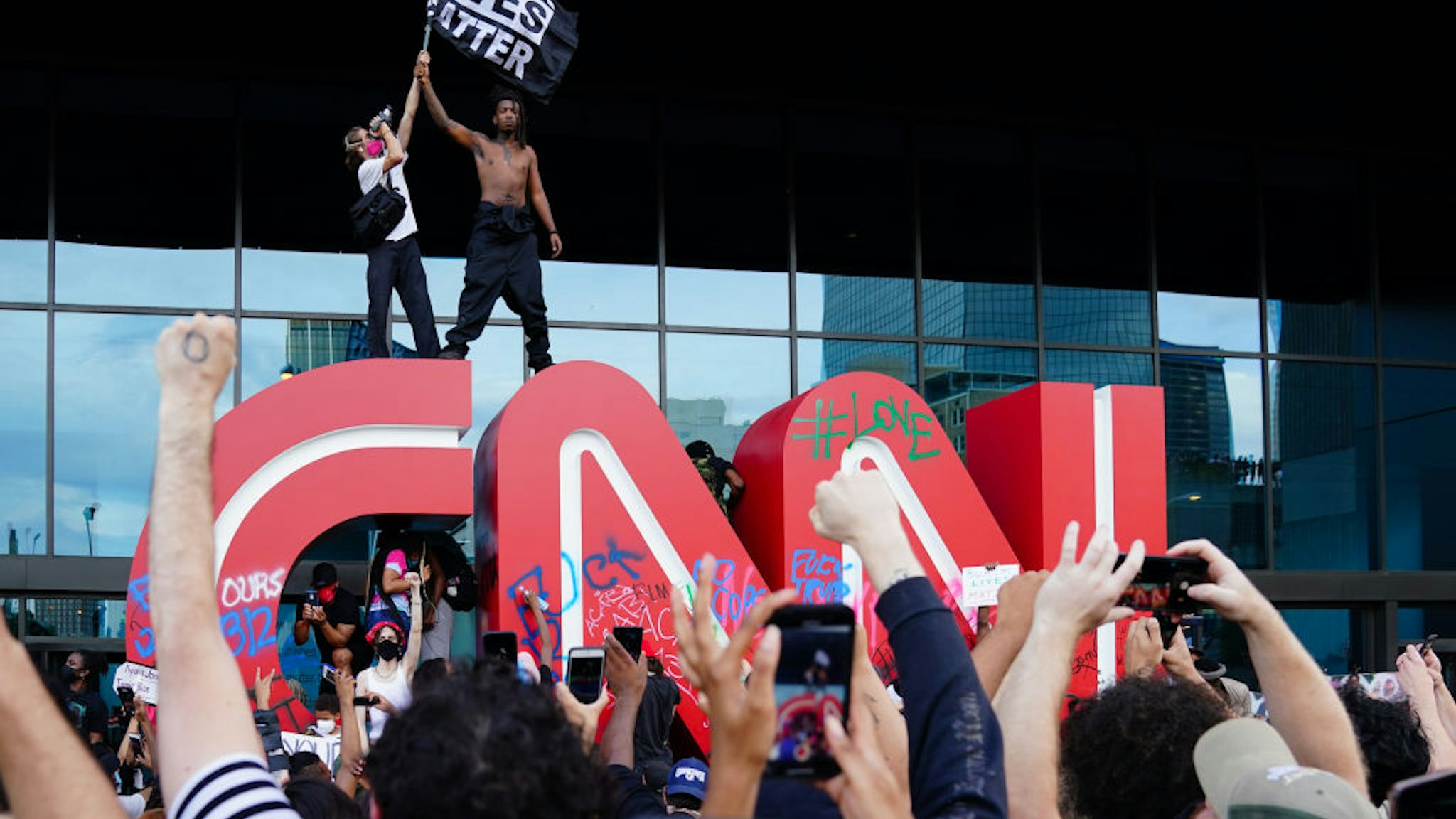 A man waves a Black Lives Matter flag atop the CNN logo during a protest in response to the police killing of George Floyd outside the CNN Center on May 29, 2020 in Atlanta, Georgia.