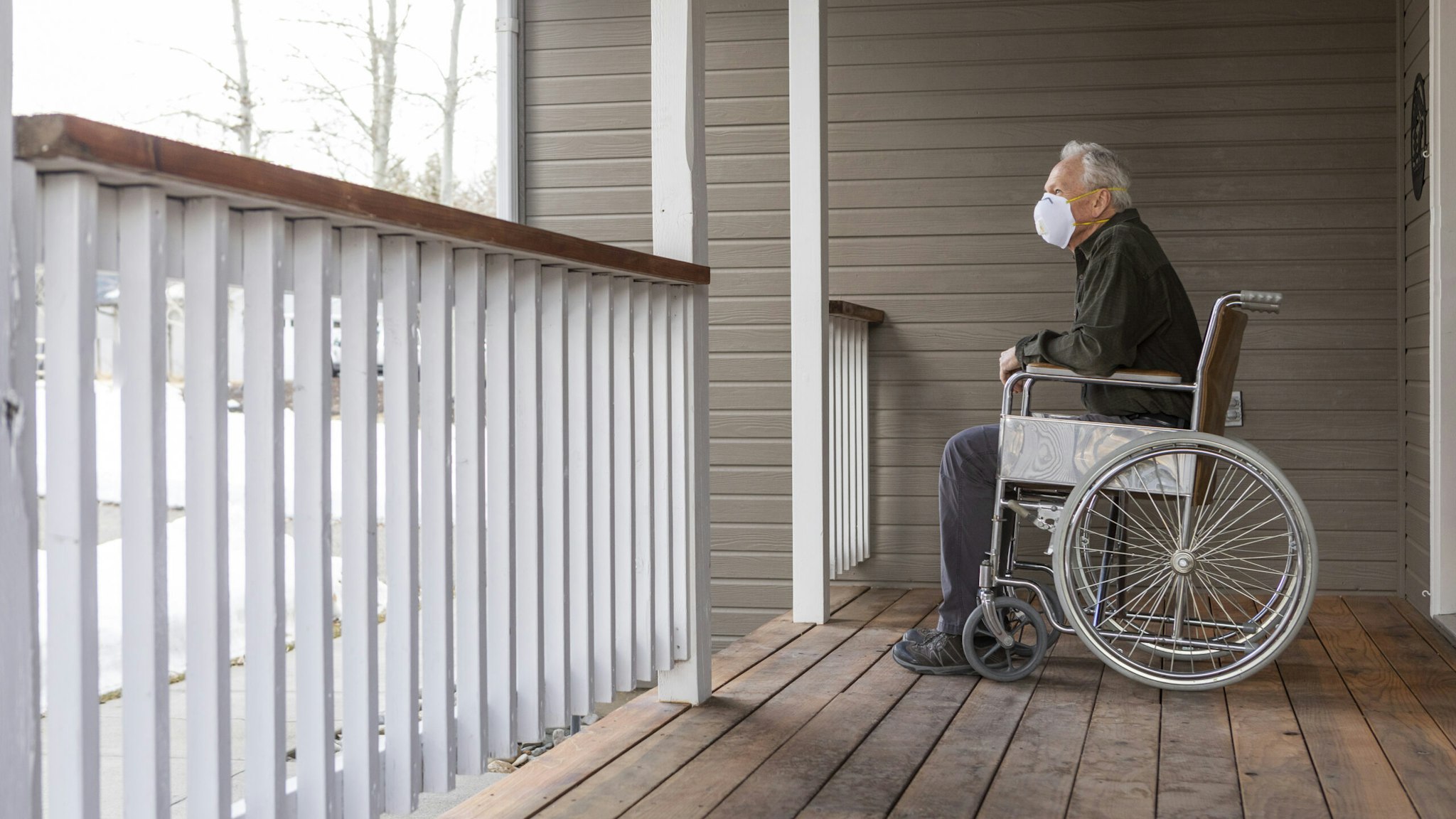 Senior man in wheelchair wearing protective mask to prevent coronavirus transmission on porch - stock photo