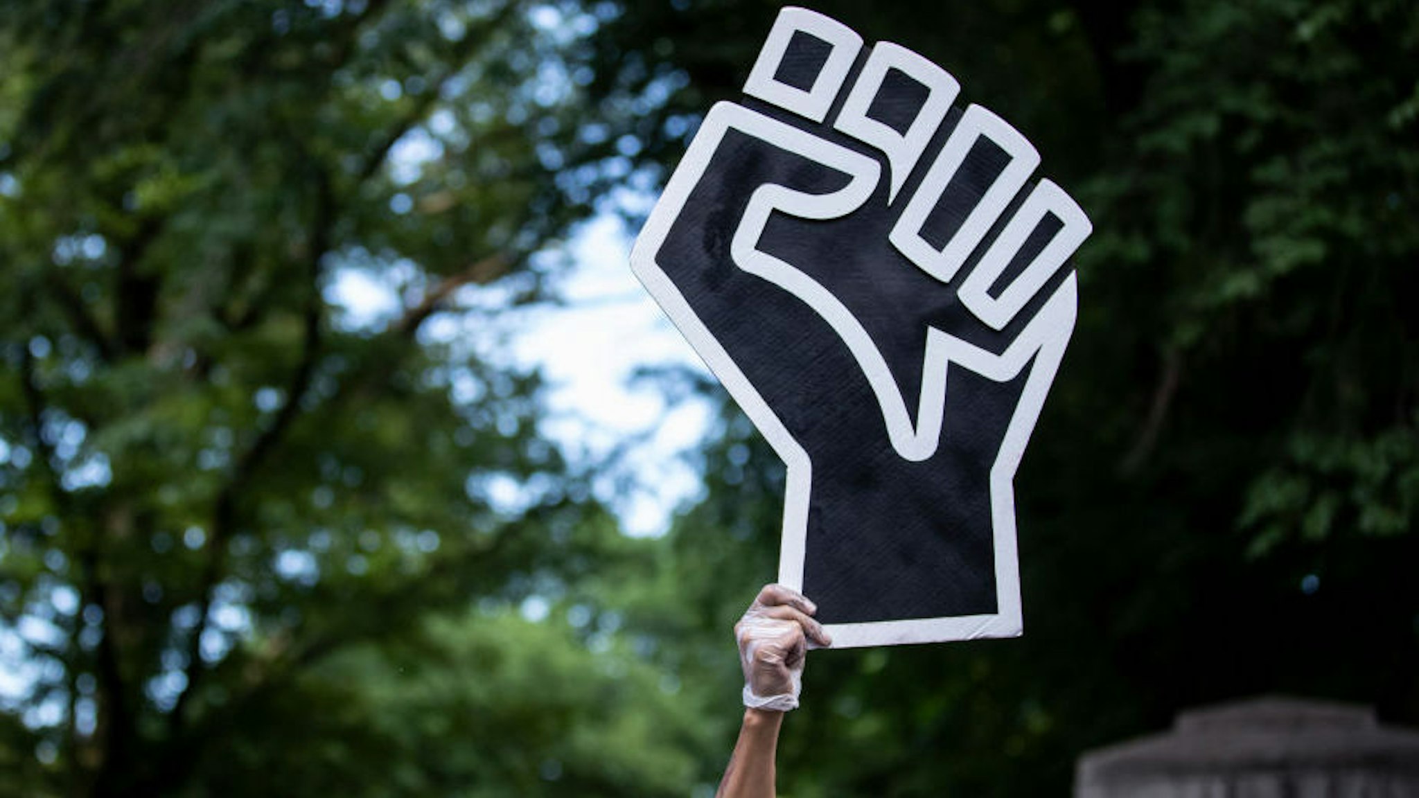 A protester wearing a mask holds a large black power raised fist in the middle of the crowd that gathered at Columbus Circle.