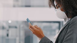 COVID Shot of a young businesswoman wearing a mask and using a smartphone in a modern officeShot of a young businesswoman wearing a mask and using a smartphone in a modern office