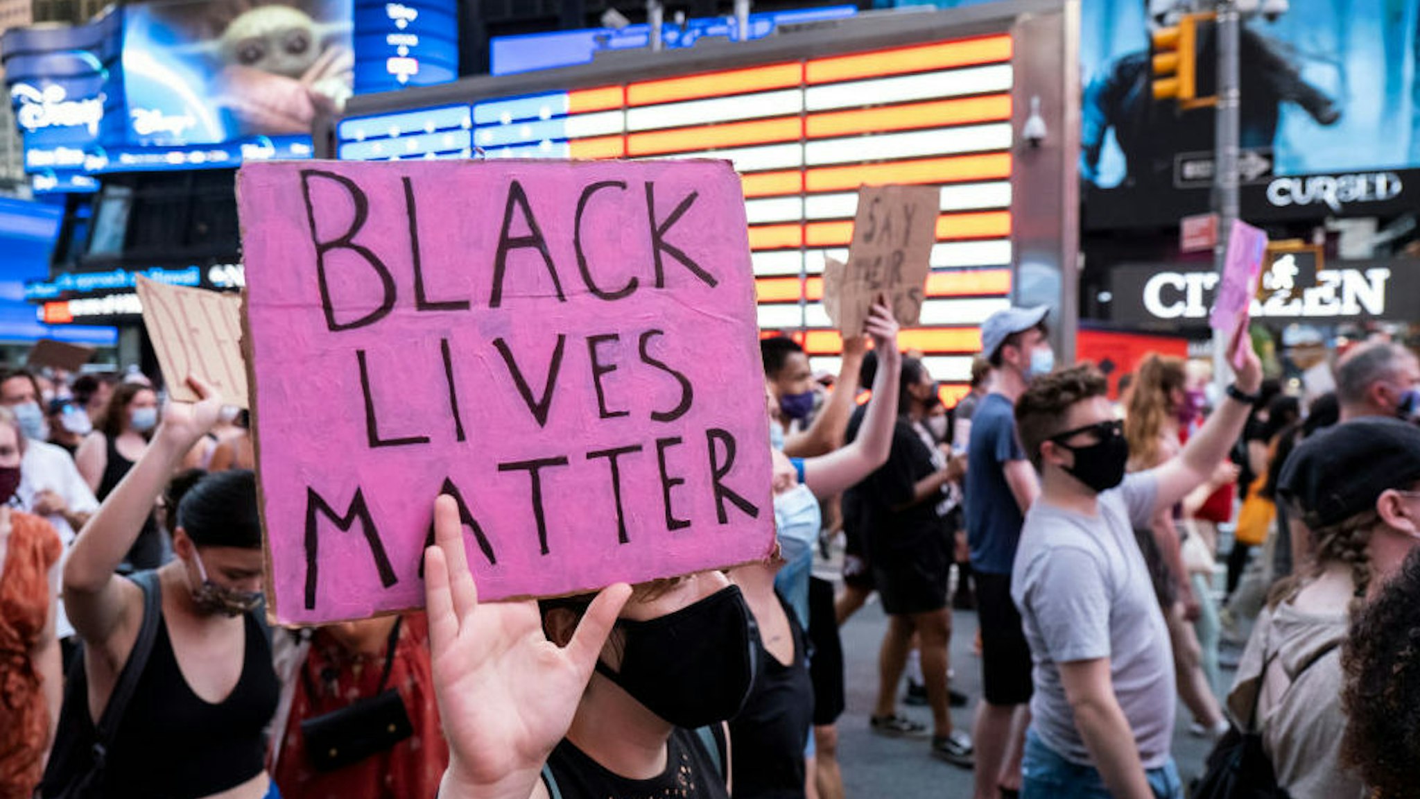 A protester holds a sign that says, "Black Lives Matter" as the crowd of hundreds pass the Jumbotron of the American Flag in Times Square New York in support of Black Women.