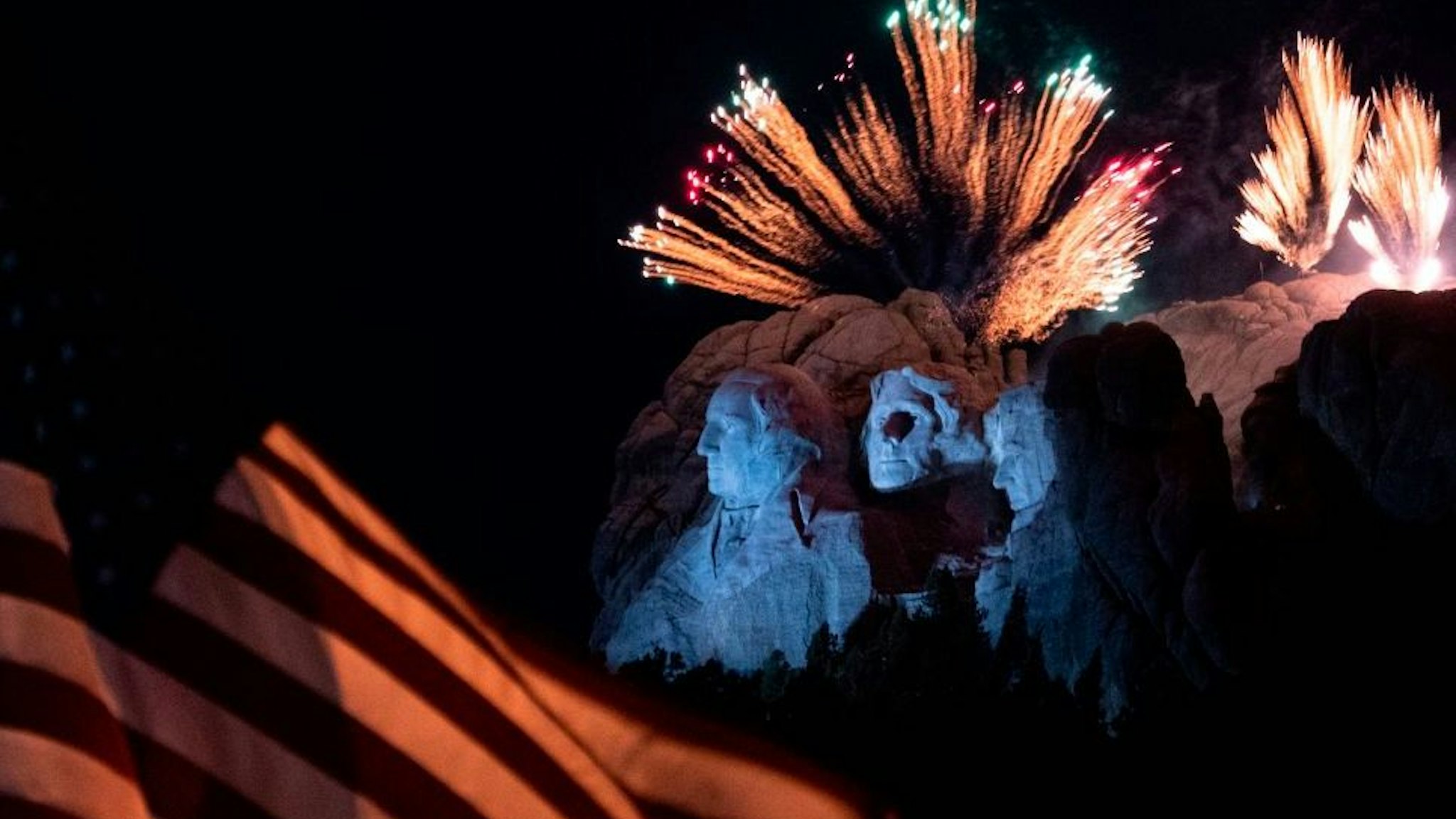 A US flag flies as fireworks explode above the Mount Rushmore National Monument during an Independence Day event attended by the US president in Keystone, South Dakota, July 3, 2020. (Photo by ANDREW CABALLERO-REYNOLDS / AFP)