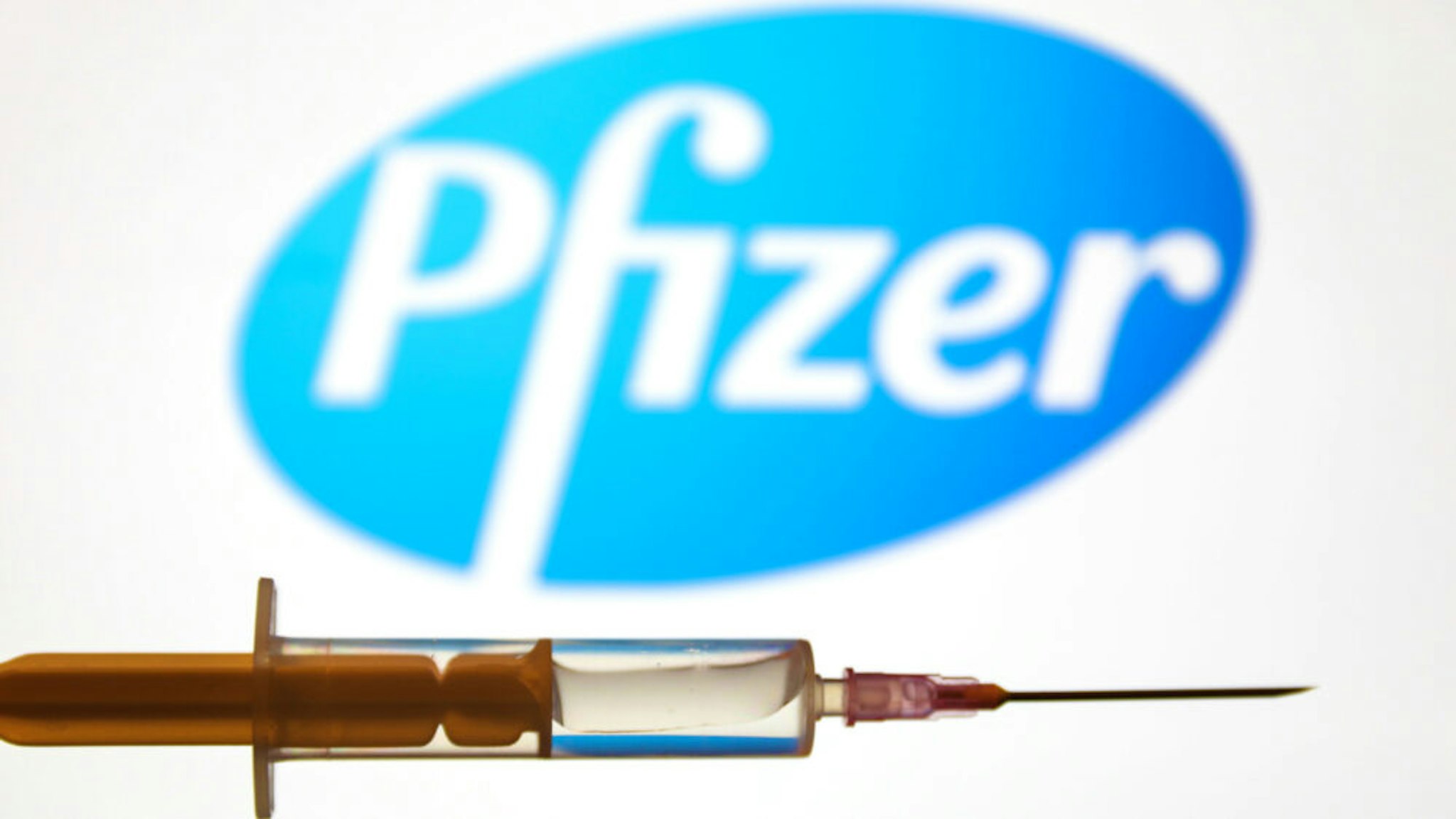 Medical syringe is seen with Pfizer company logo displayed on a screen in the background in this illustration photo taken in Poland on June 16, 2020.