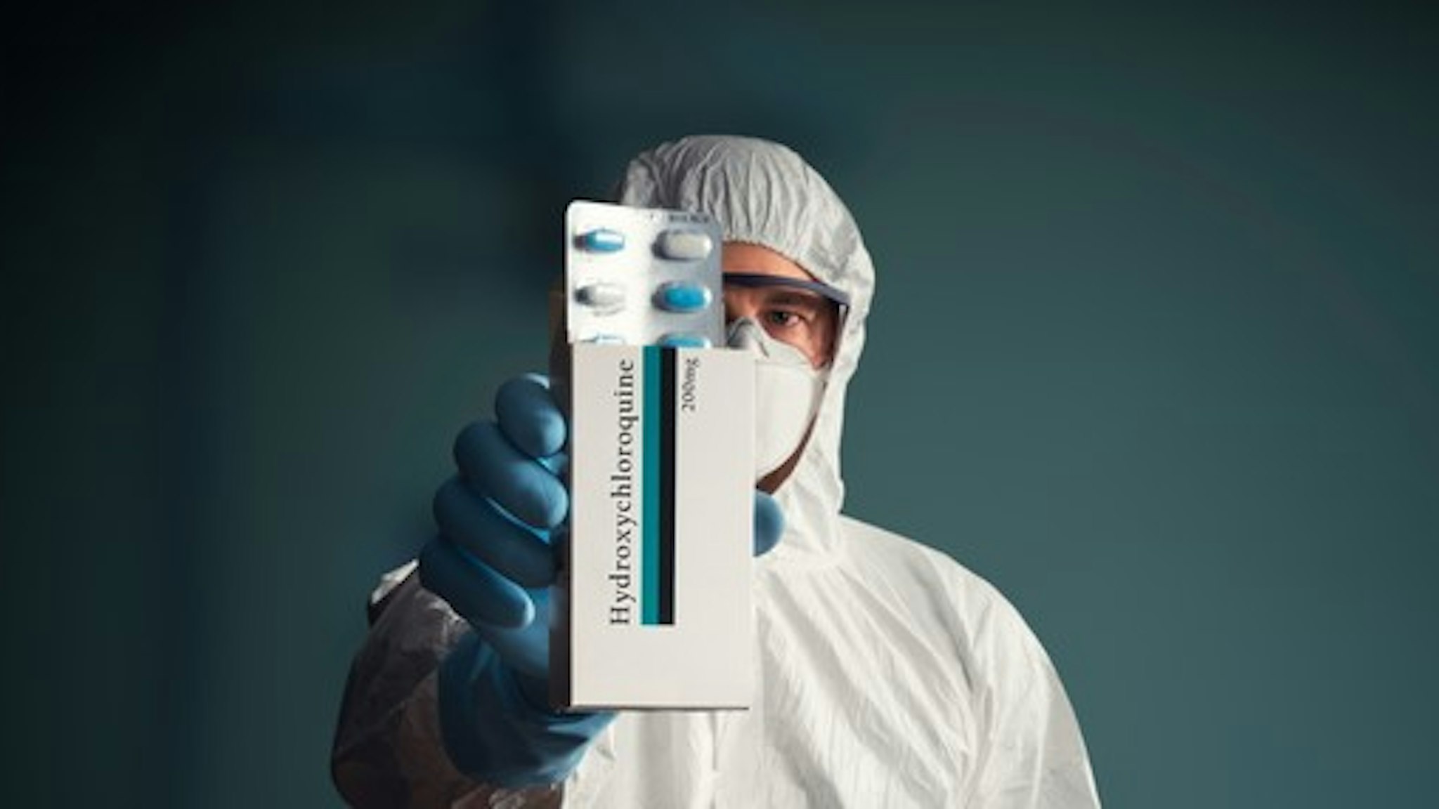 Medical worker in full protective suit holding hydroxychloroquine drug tablets