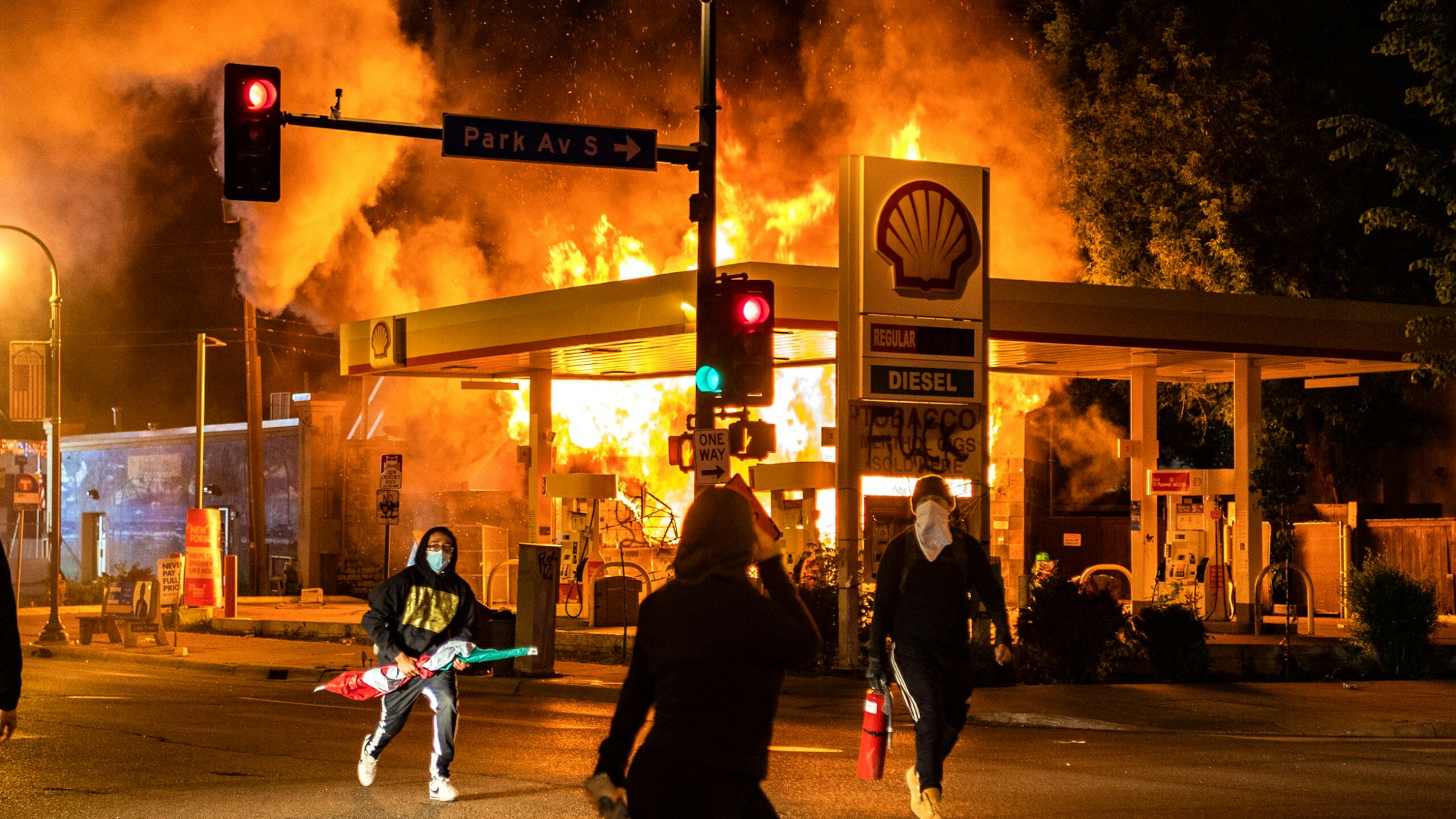 MINNEAPOLIS, MN - MAY 29: Protesters walk past a gas station on the corner of Park Ave S and E. Lake St that is on fire on Friday, May 29, 2020, in Minneapolis, MN. Protests in the wake of the death of George Floyd while in police custody swept country overnight Thursday.