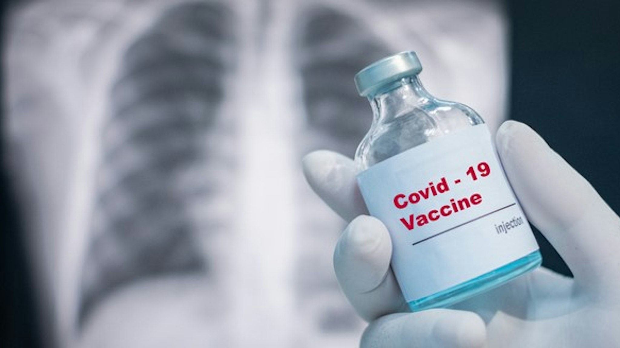 Doctor's hand holding a covid-19 vaccine vial on Chest x-ray background