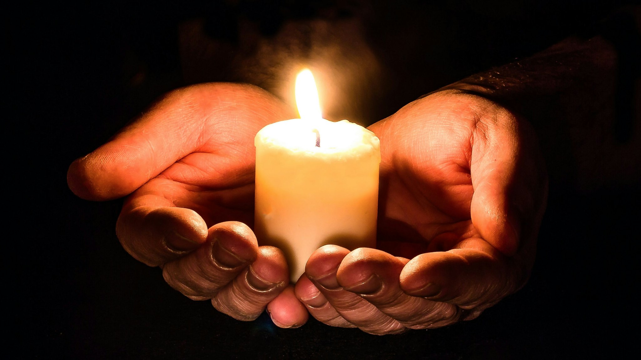 Cropped Hands Holding Illuminated Candle Against Black Background - stock photo.