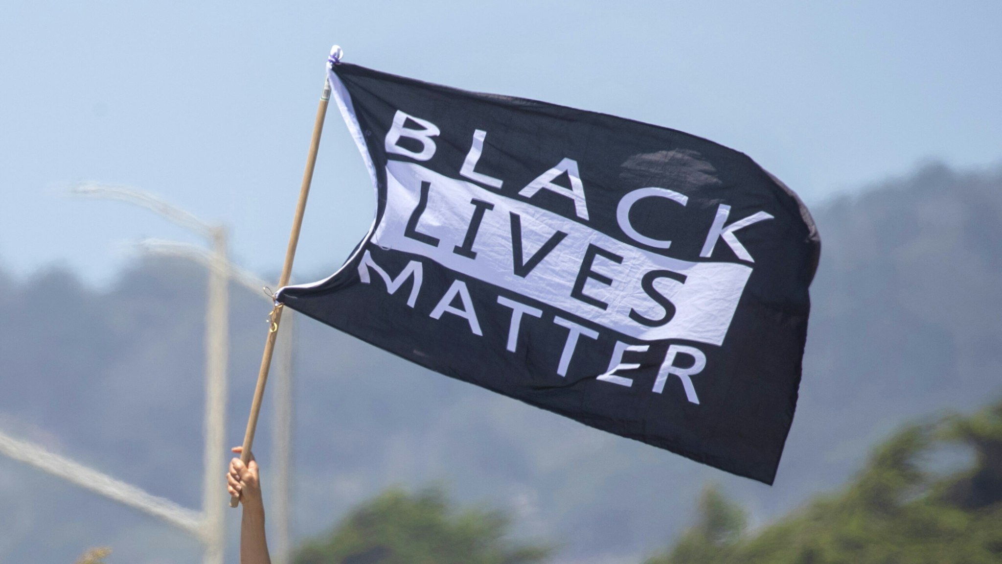 SAN FRANCISCO, CA.- JUNE 2: Black Lives Matter marchers are greeted by a flag-waving supporter on the Great Highway in San Francisco, Tuesday, June 2, 2020.