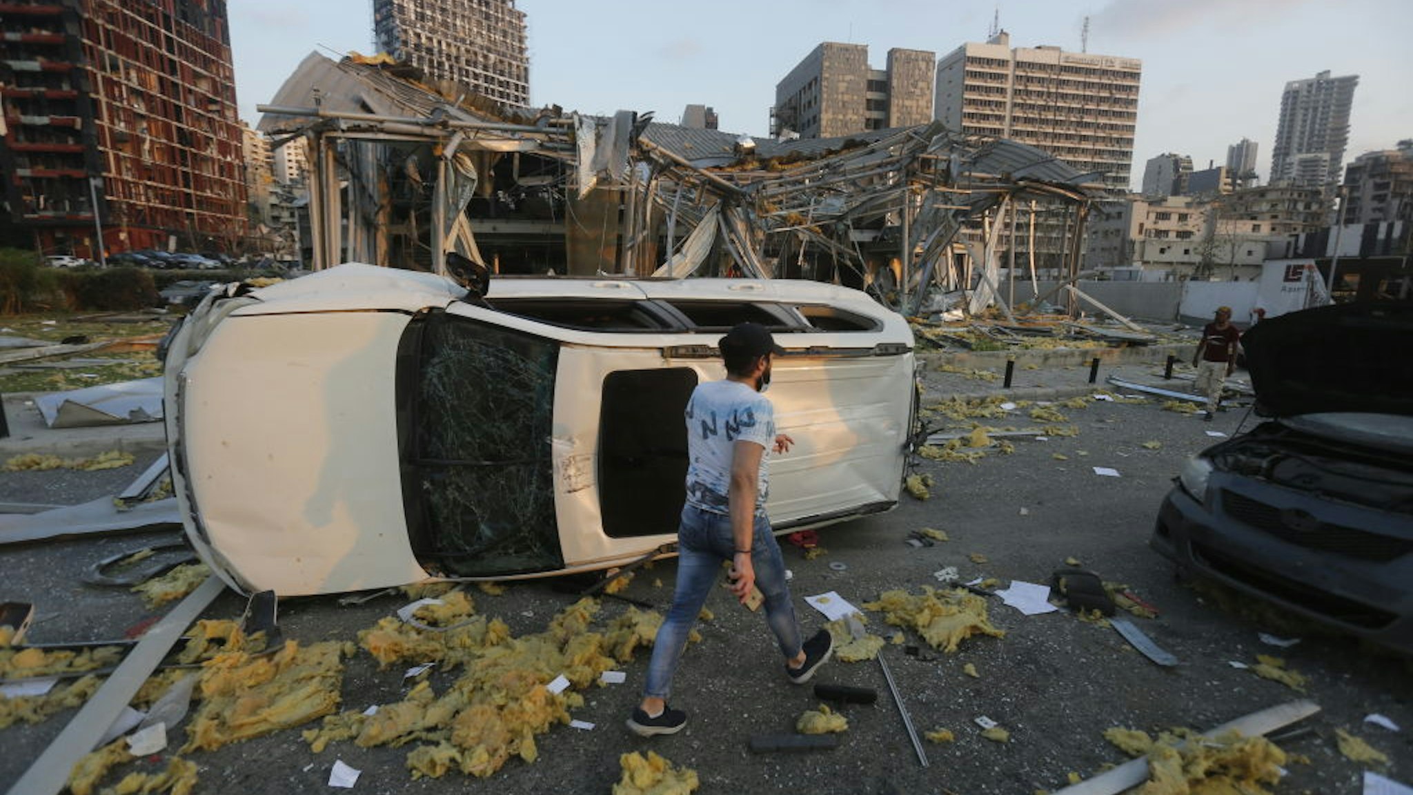 BEIRUT, LEBANON - AUGUST 04: A man walks by an overturned car and destroyed buildings on August 4, 2020 in Beirut, Lebanon. At least 50 people were killed and thousands more injured when two explosions occurred near the Lebanese capital's port area.