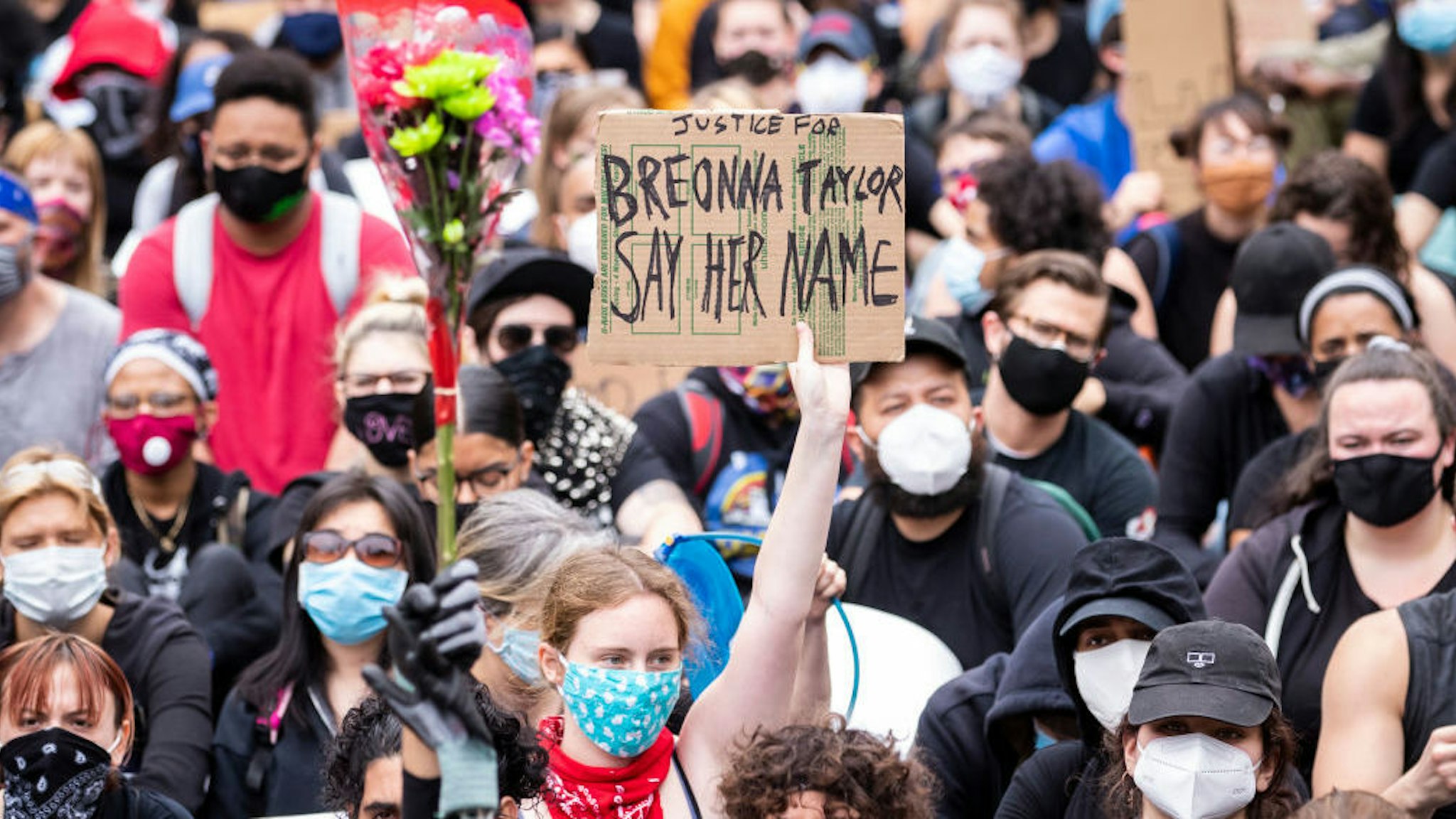 A white protester wearing a mask holds a sign that says, "Justice for Breonna Taylor Say Her Name" while another protester holds a bouquet of flowers next to them among the large crowd in Foley Square. On July 30, 2020, Oprah Magazine announced that they were going to feature Breonna Taylor on the cover. This is the first time someone other than Oprah has been on the cover of Oprah Magazine in its 20 year history. On July 28, 2020 Nikki Stone a homeless transgender woman was abducted off the streets and taken onto an unmarked van and arrested. Protesters took to the streets across America after the killing of George Floyd at the hands of a white police officer Derek Chauvin that was kneeling on his neck during his arrest as he pleaded that he couldn't breathe. The protest are attempting to give a voice to the need for human rights for African American's and to stop police brutality against people of color. Many people were wearing masks and observing social distancing due to the coronavirus pandemic. Leaders of the protest were clear that they wanted it to be a peaceful protest in light of nights of unrest looting and destruction. Photographed in the Manhattan Borough of New York on June 02, 2020, USA. (Photo by Ira L. Black/Corbis via Getty Images)