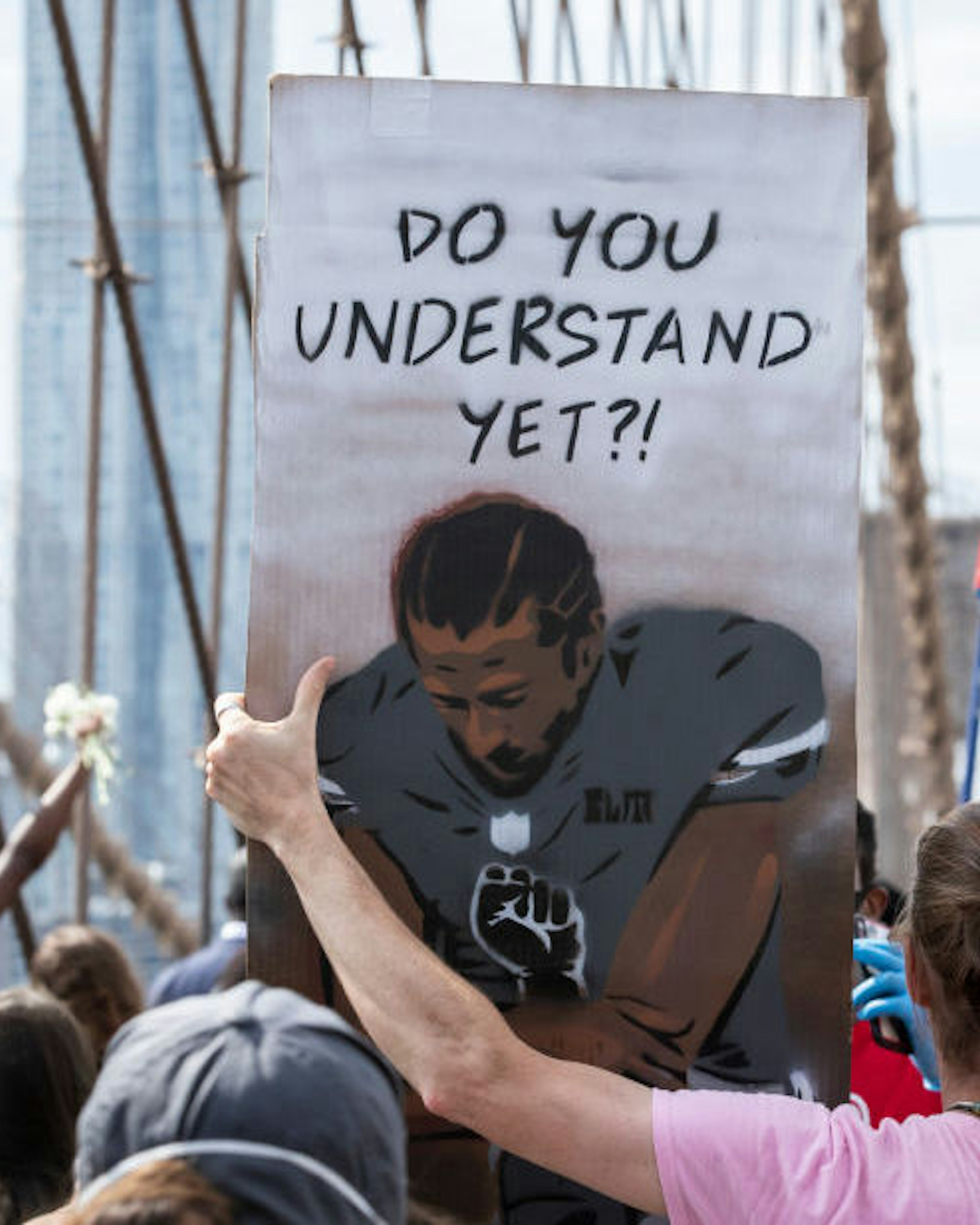 A Caucasian protester holds a sign that says,"Do You Understand Yet?" with a picture of Colin Kaepernick, former quarterback for the San Francisco 49ers, taking a knee with a Black Power Fist on in the middle of his jersey with the Arches of the Brooklyn Bridge behind them as they walk across the Brooklyn Bridge in protest of police racism. Protesters walked from Brooklyn to Manhattan after a memorial ceremony in Brooklyn with Terrence Floyd, brother of George Floyd. Protesters have taken to the streets across America and around the world after the killing of George Floyd at the hands of a white police officer Derek Chauvin that was kneeling on his neck during his arrest as he pleaded that he couldn't breathe. The protest are attempting to give a voice to the need for human rights for African American's and to stop police brutality against people of color. Many people were wearing masks and observing social distancing due to the coronavirus pandemic. Terrence Floyd echoed the word of peaceful protest saying that violent protests are overshadowing What's Going On. New York City remains in a curfew as an answer to nights of unrest looting and destruction. Photographed in the Manhattan Borough of New York on June 04, 2020, USA. (Photo by Ira L. Black/Corbis via Getty Images)